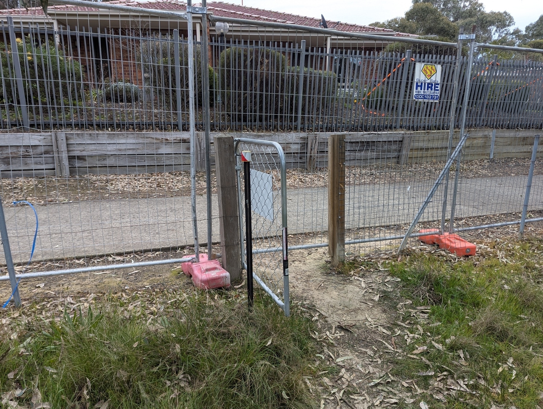 An open gate in front of a temporary fence blocking access to a path.