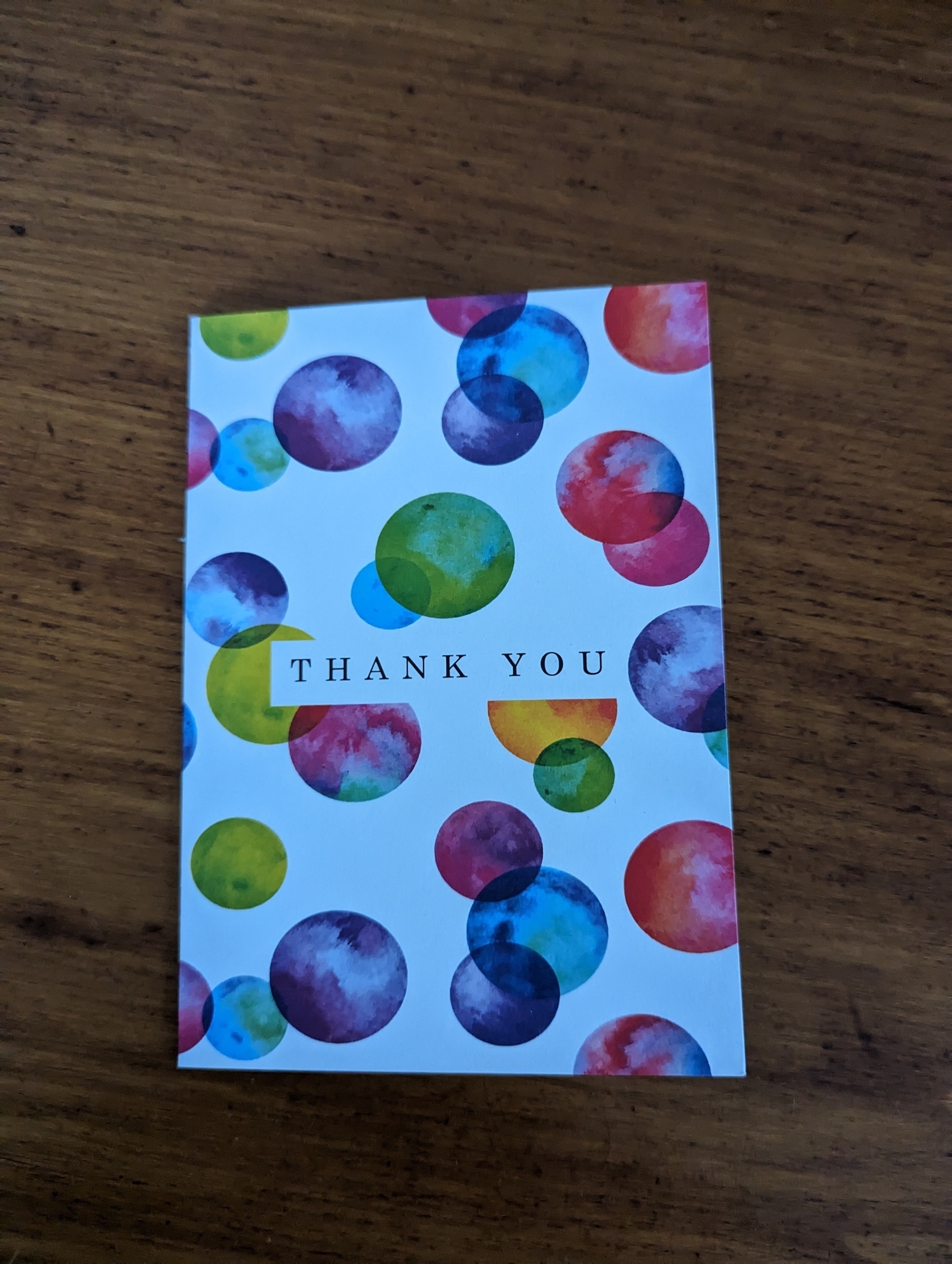 A Thank You card with coloured balloons printed on the front, on a wooden table.