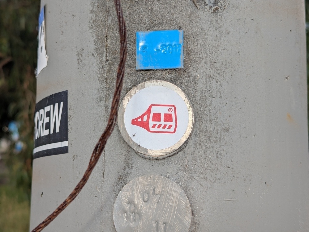 A utility pole is adorned with various stickers, including a red and white sticker of a train.