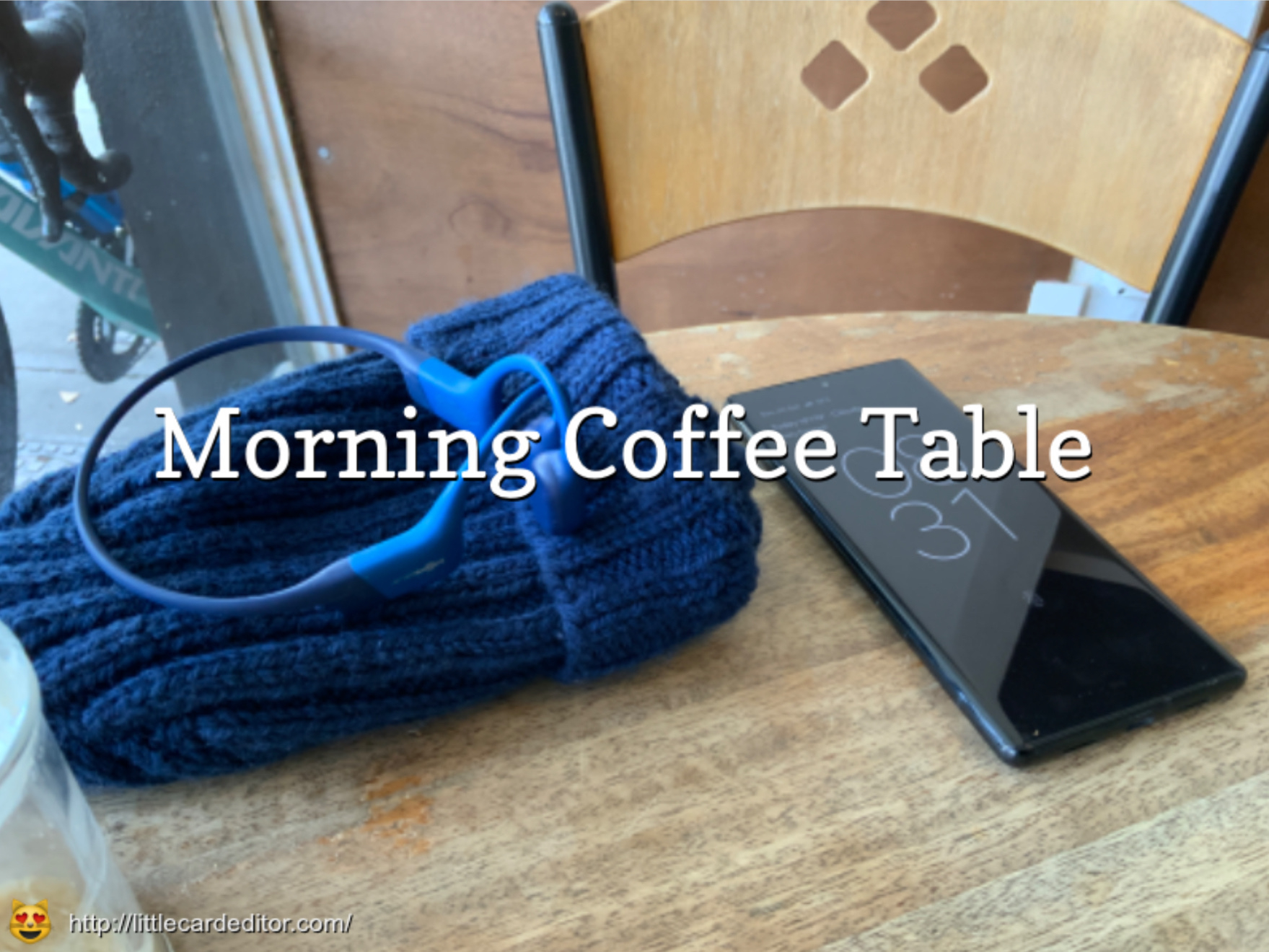 A cozy coffee table setup with a blue knitted item, blue headphones, and a smartphone displaying the time. The title ‘Morning Coffee Table’ is overlayed in the centre in a serif font.