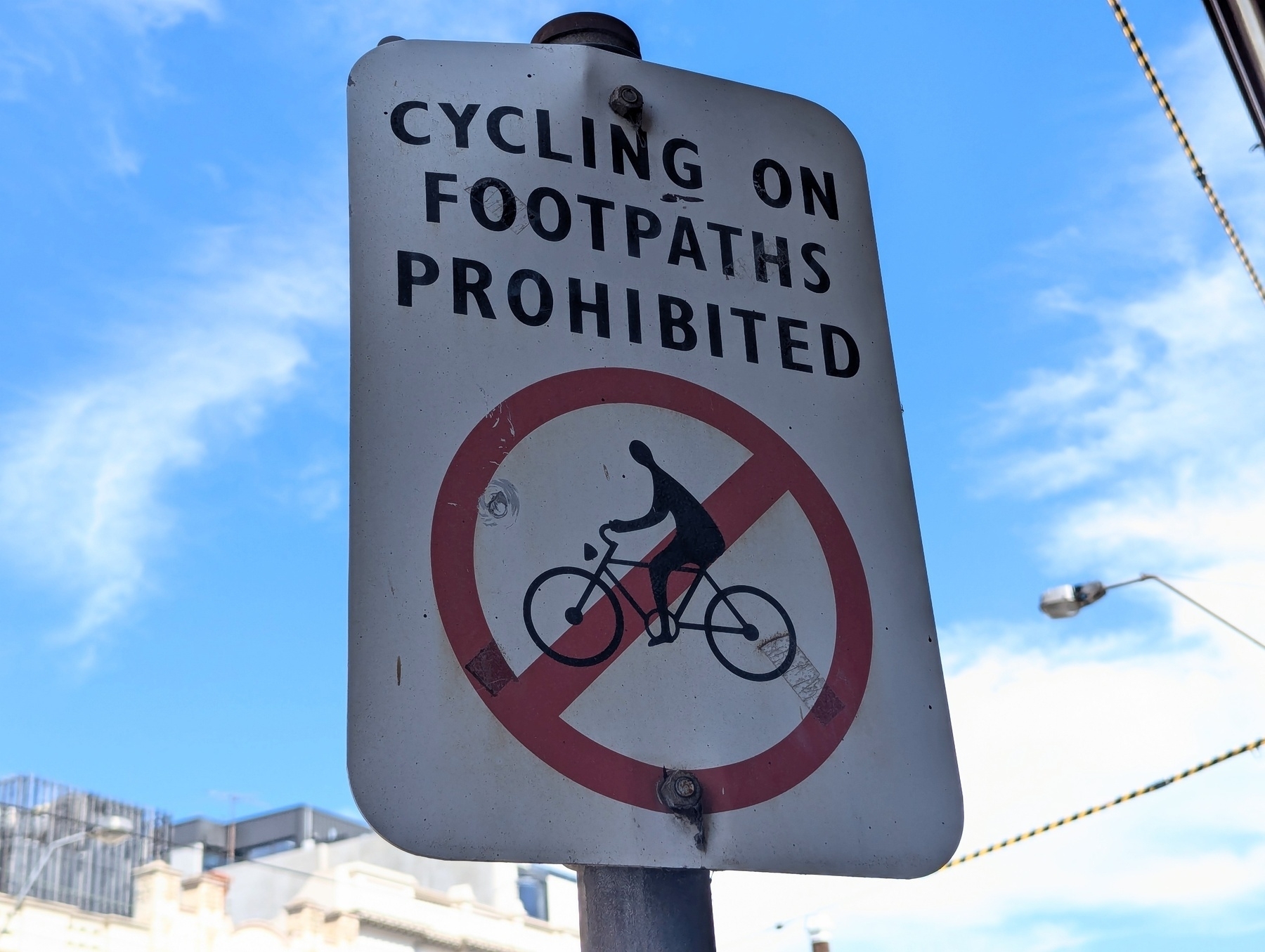 A sign indicates that cycling on footpaths is prohibited with a red circle and a line through a bicycle symbol.