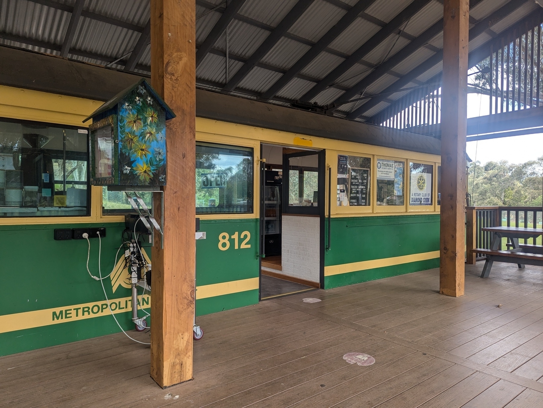 A repurposed tram is used as a cafe, featuring outdoor seating under a large covered area.