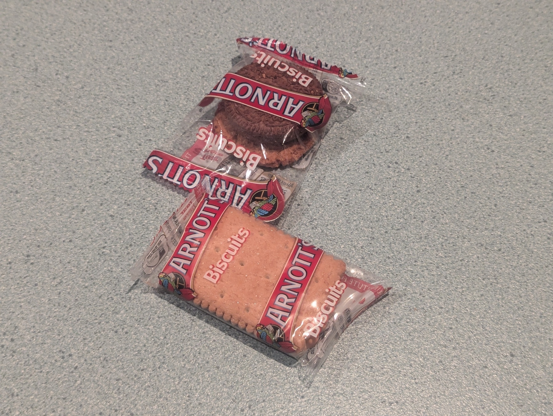 Two individually wrapped Arnott's biscuits packets are placed on a green and grey bench.