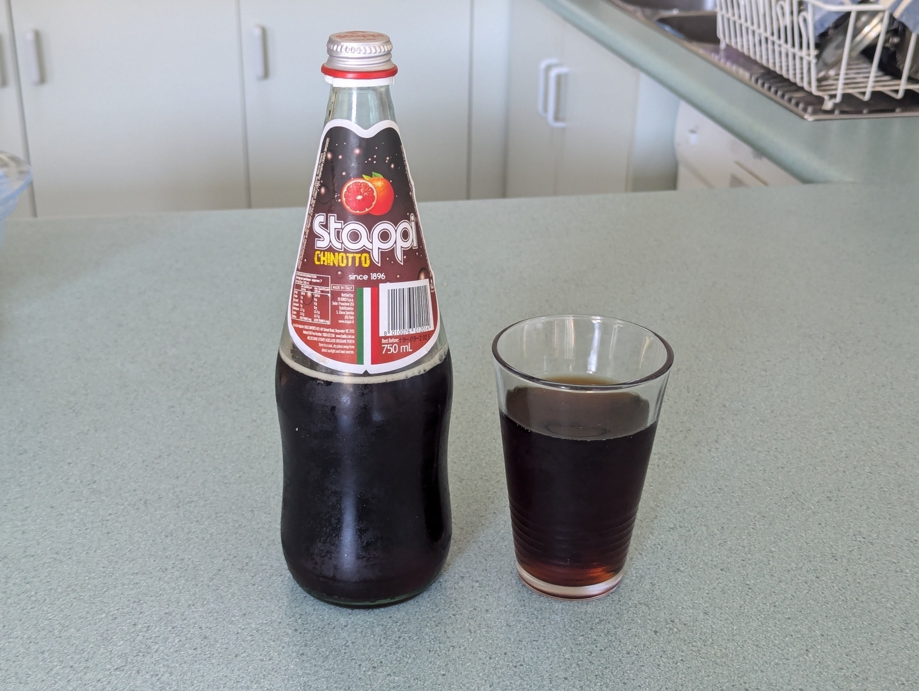 A bottle and a glass of Stappi Chinotto are placed on a kitchen benchtop.