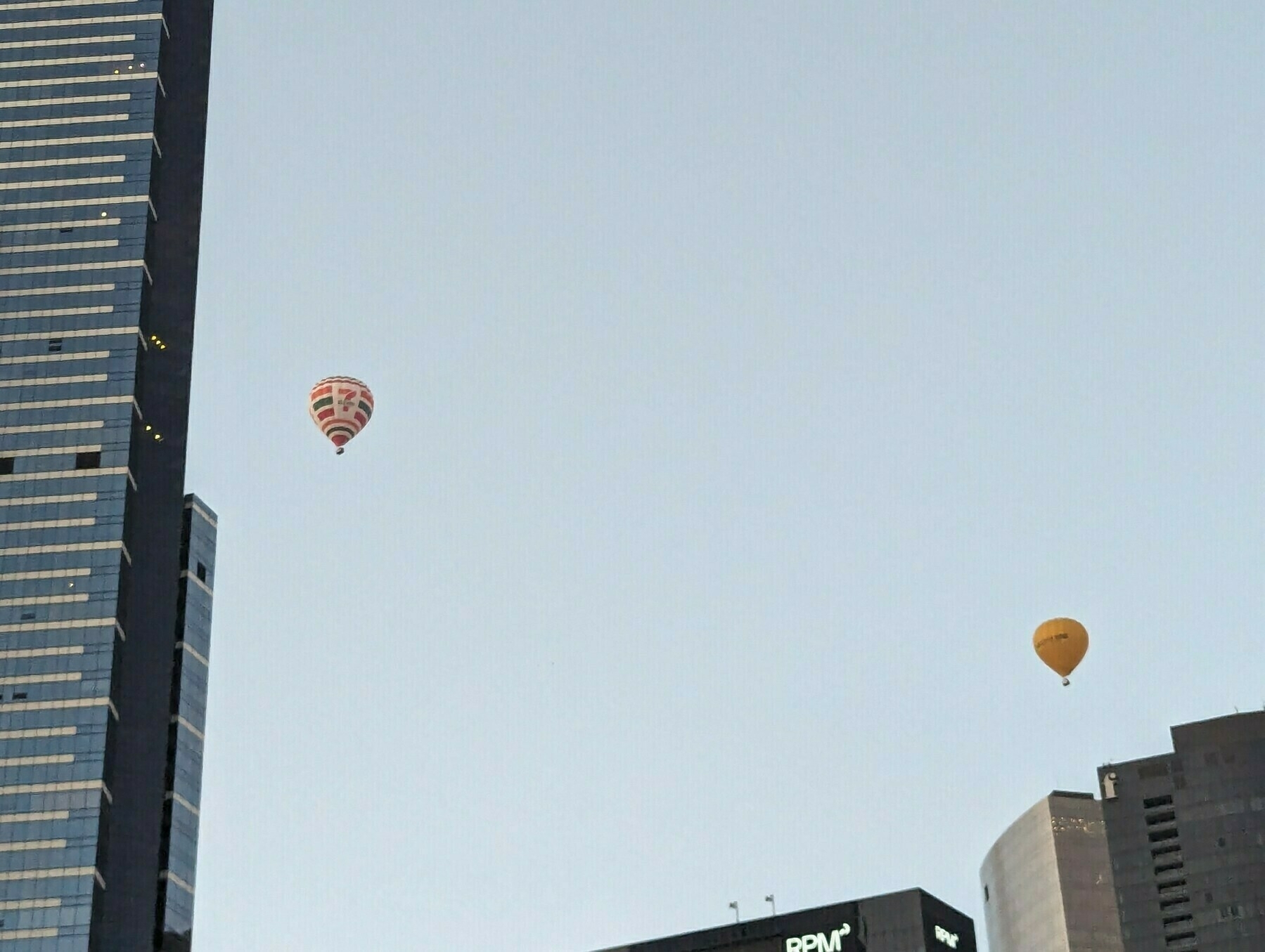 Two hot air balloons flying around skyscrapers.