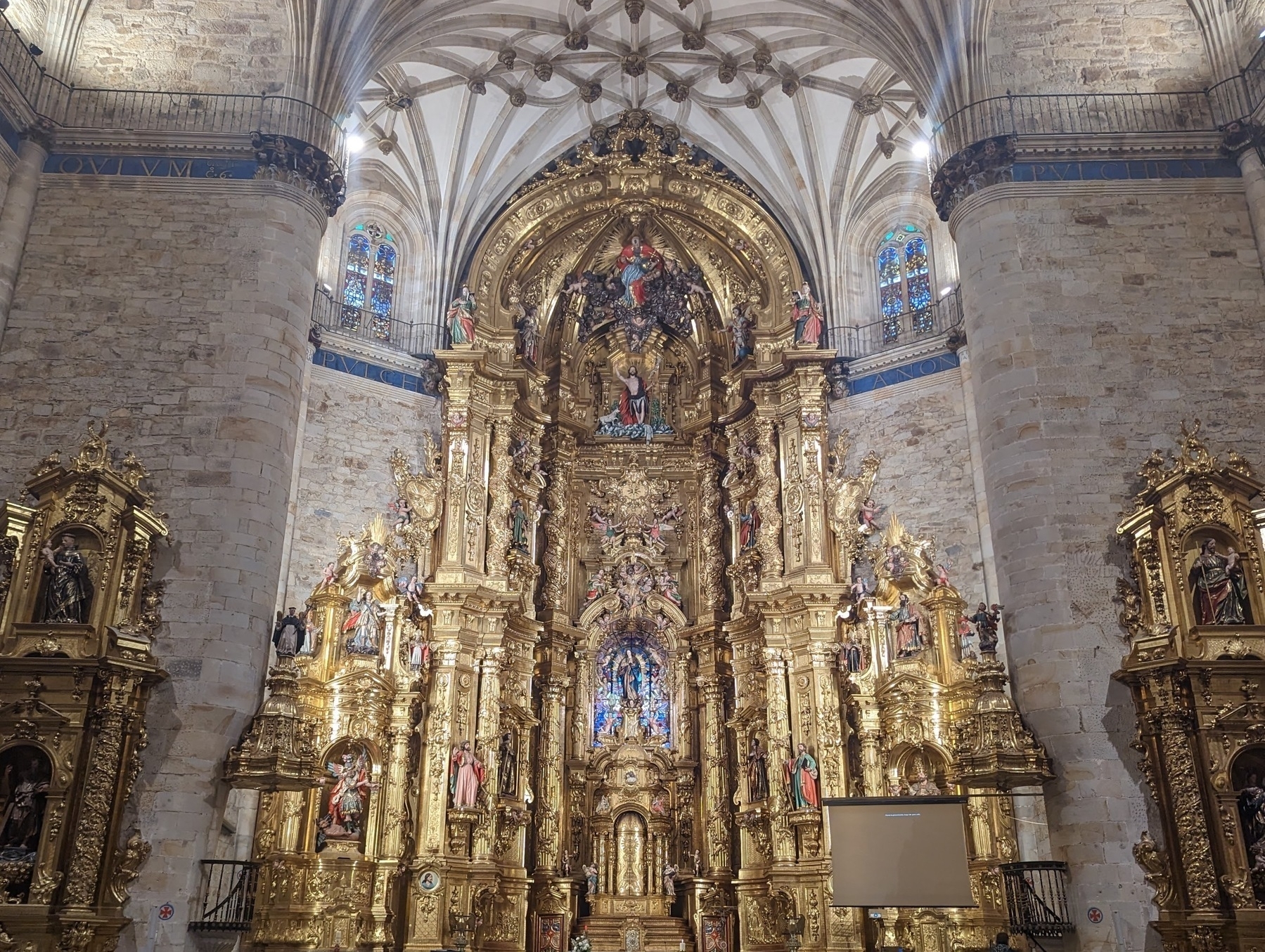 An ornate, gilded altar in a medieval Spanish church lit with sunlight and artificial light.