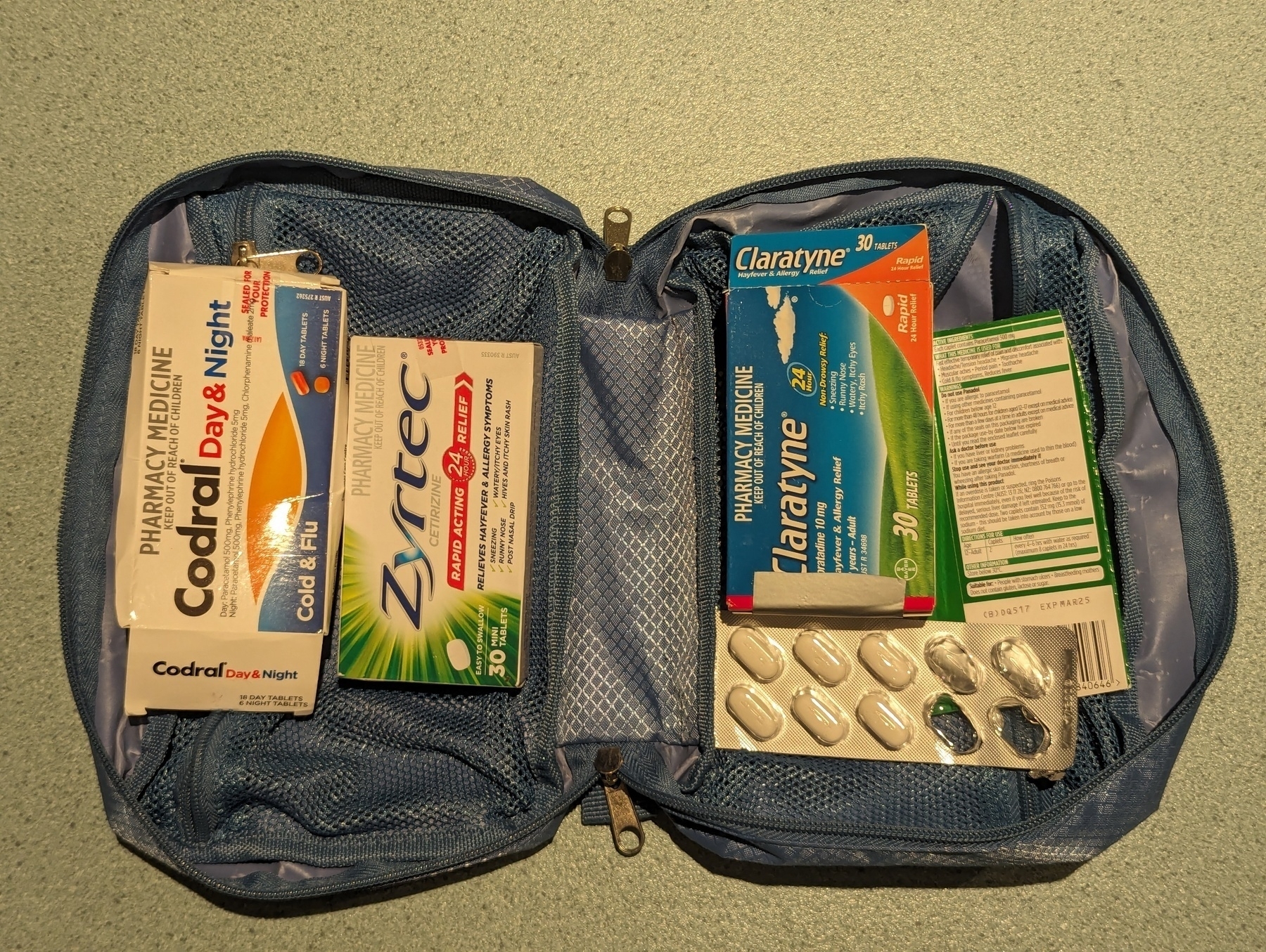 An small blue bag, opened to reveal a bunch of over the counter medication like cold and flu tablets, pain killers, etc.