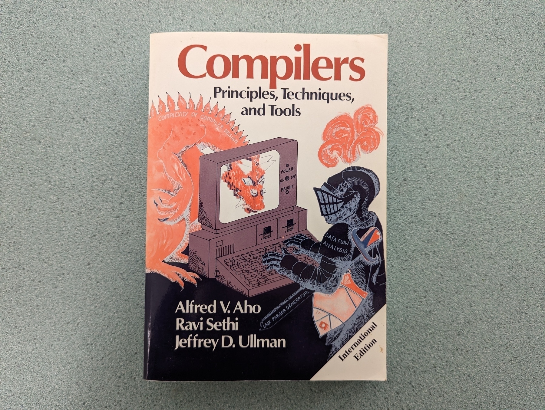Auto-generated description: A book titled Compilers: Principles, Techniques, and Tools by Alfred V. Aho, Ravi Sethi, and Jeffrey D. Ullman, often referred to as the Dragon Book, is lying on a textured surface.