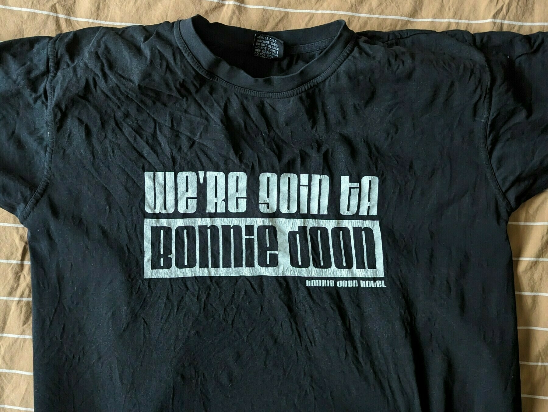 A black T-shirt is displayed with the text 'WE'RE GOIN TA BONNIE DOON' printed on the front in bold white letters, with the line Bonnie Doon Hotel below it on the right.