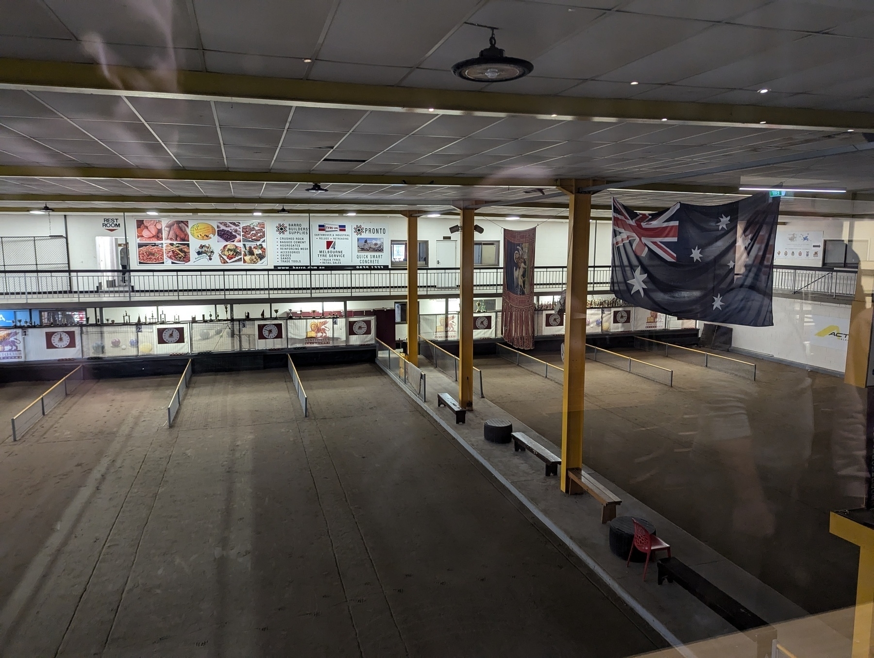 An indoor sports facility features several lanes and flags, including the Australian flag, hanging from the ceiling, with menu boards and photos displayed on the walls.