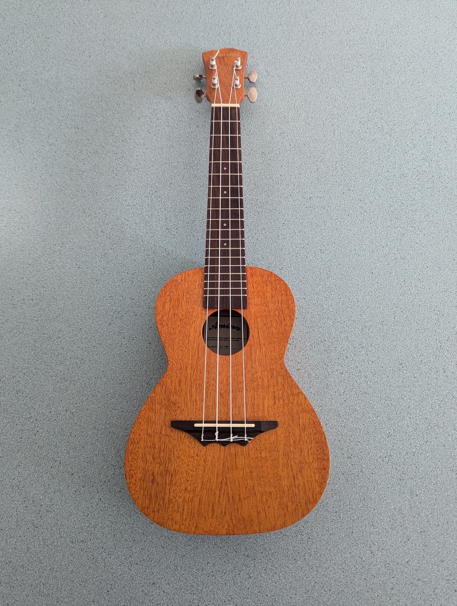 Auto-generated description: A small, wooden ukulele with four strings is lying on a textured, light blue surface.