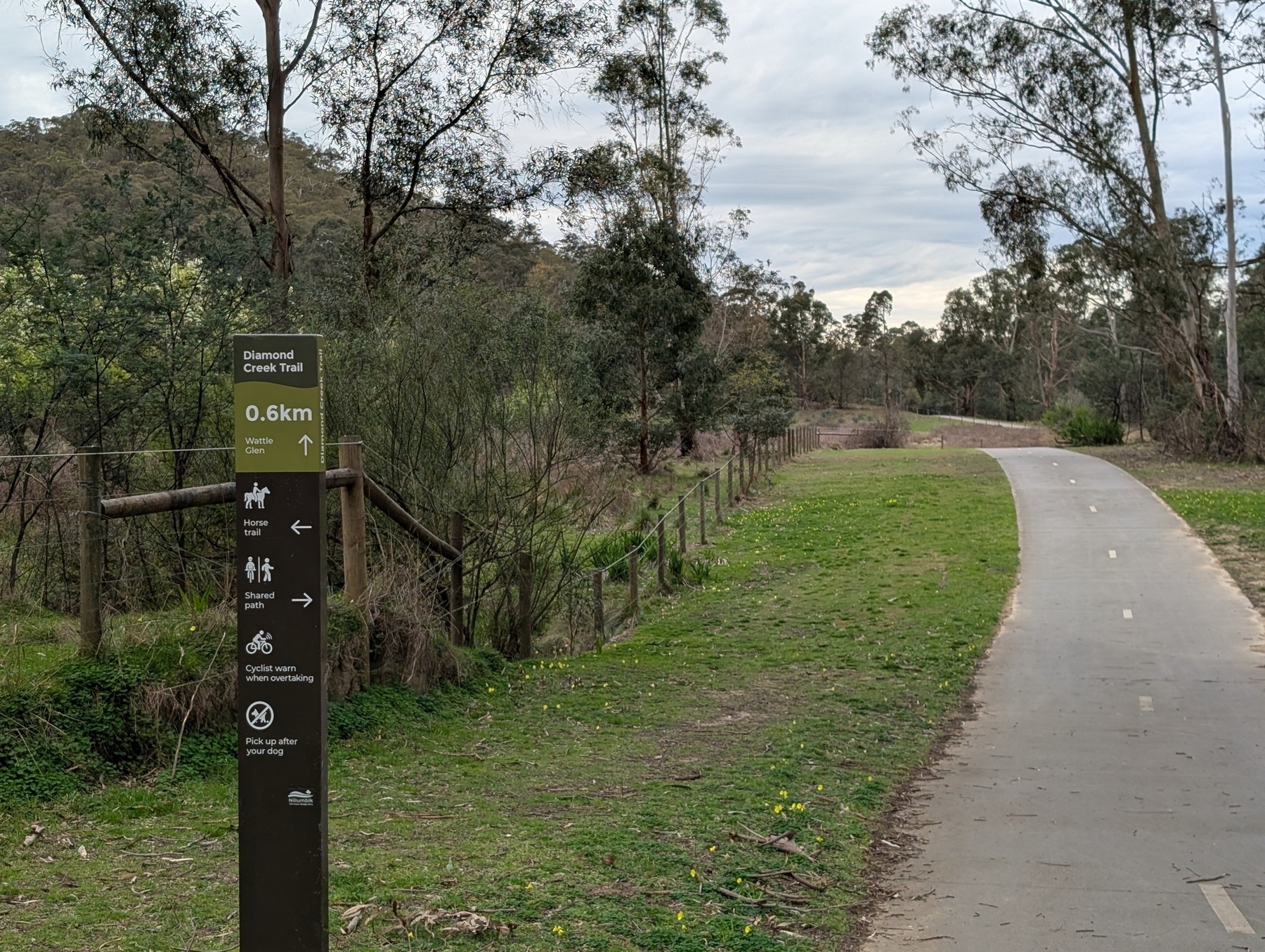 A paved trail winds through a grassy park area with a directional sign indicating it's the Diamond Creek Trail.