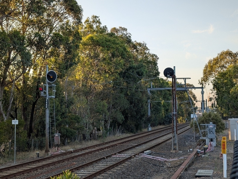 Railway tracks run through a wooded area with signal lights visible along the path.