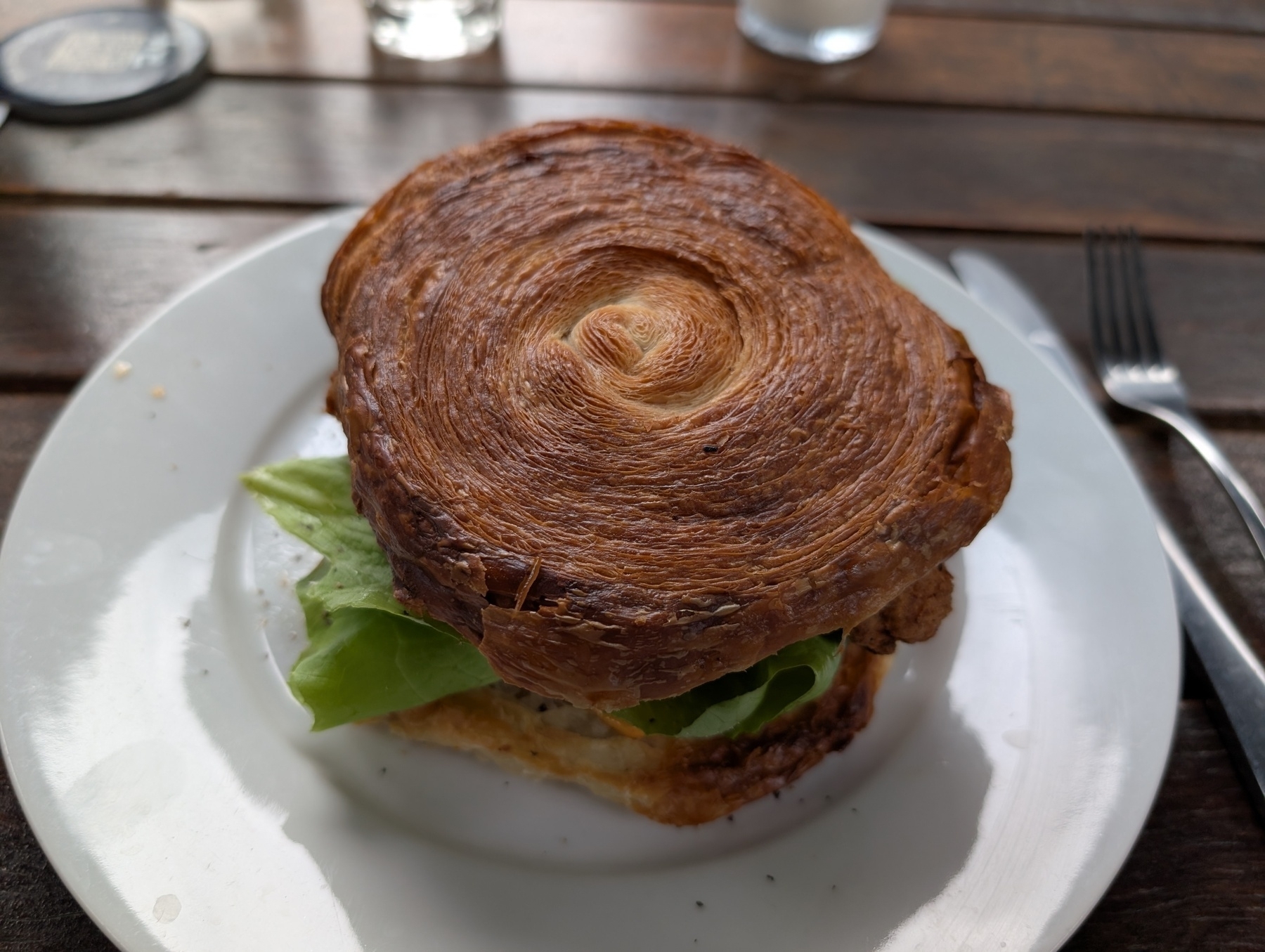 A sandwich is served on a plate with a flaky, croissant-like bun and green lettuce inside.