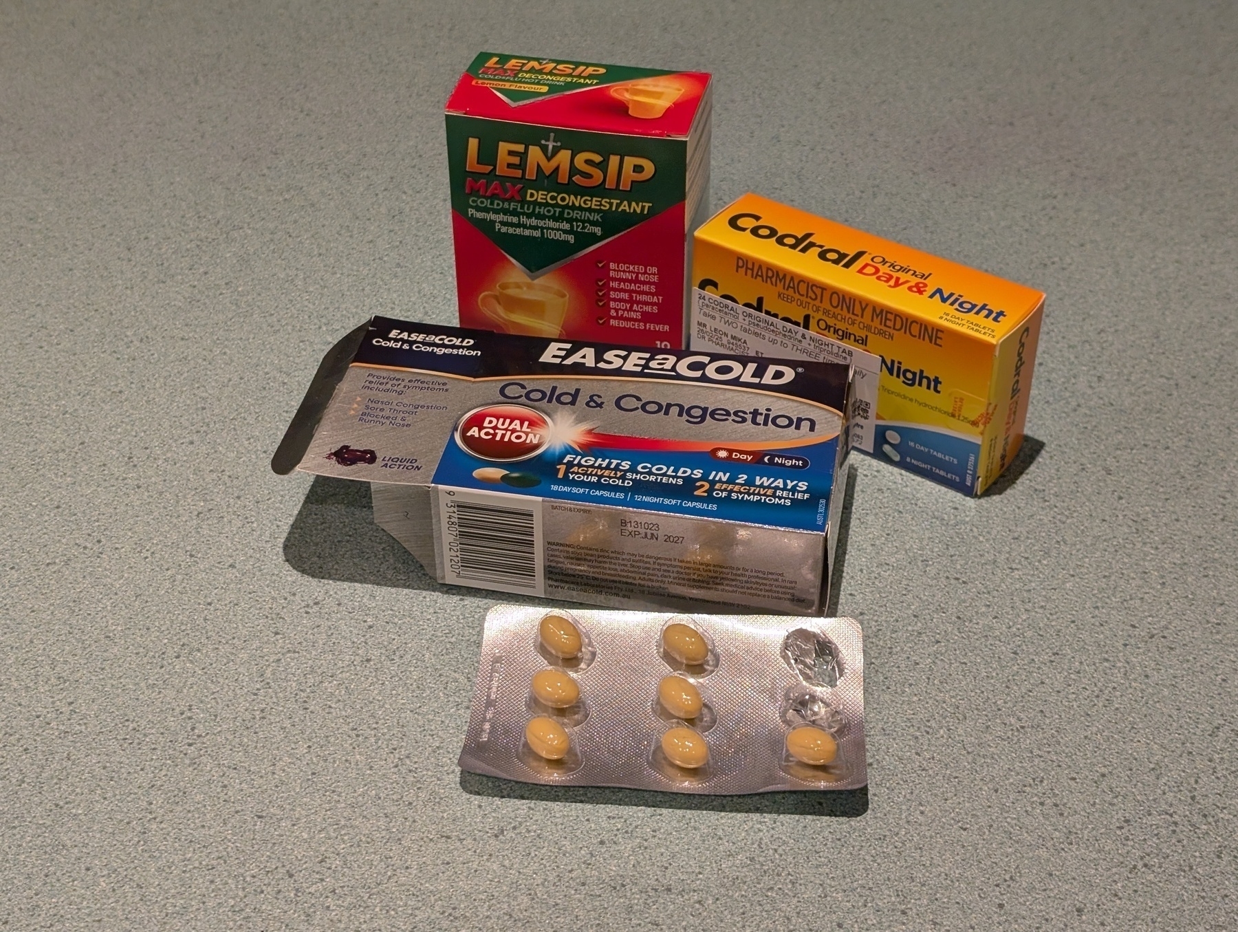 Boxes of cold and flu tablets and drinking sashes layed out on a bench.