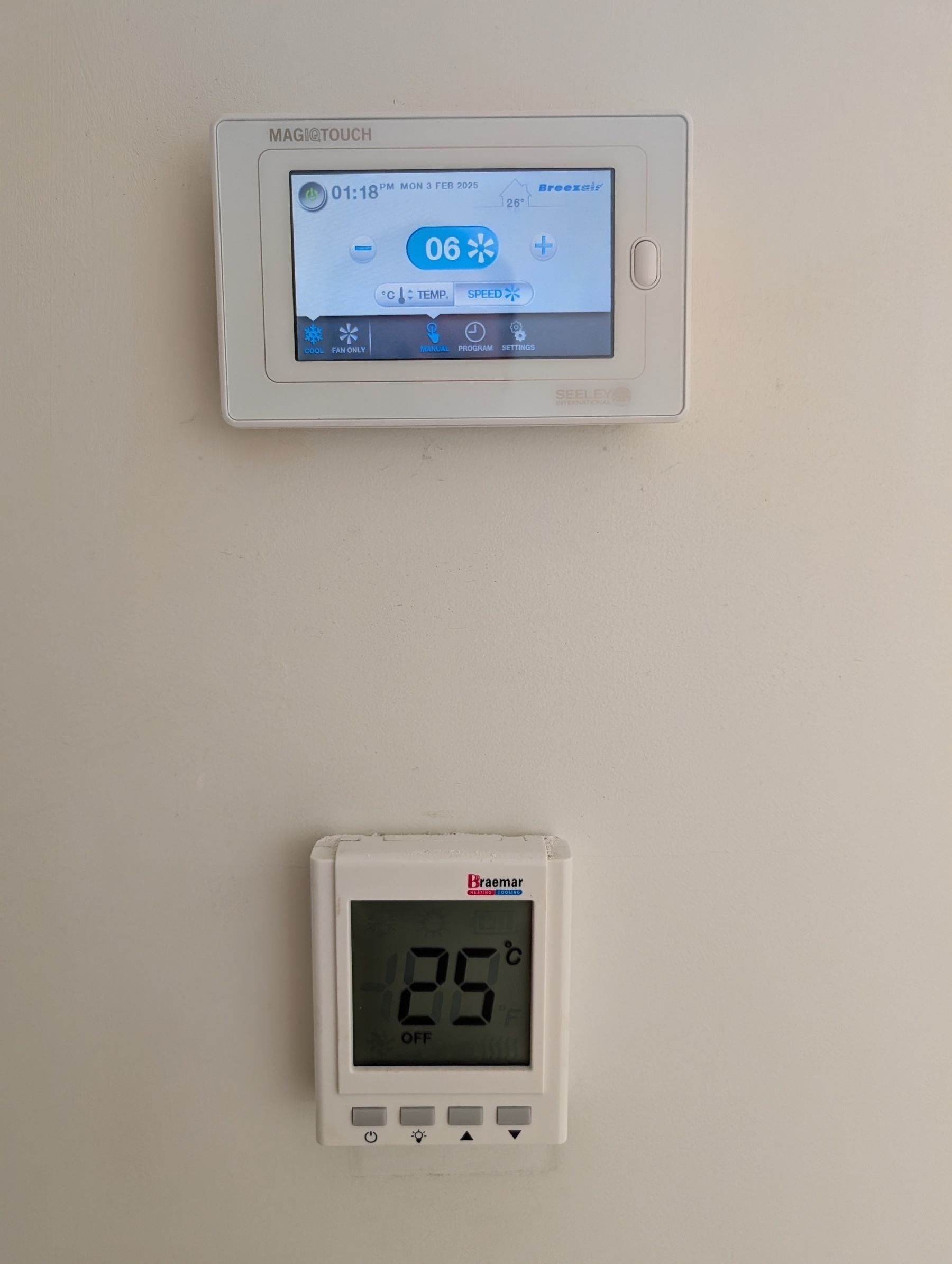 A digital thermostat showing a temperature of 25°C is mounted below another digital control panel with a touchscreen showing various settings displayed.