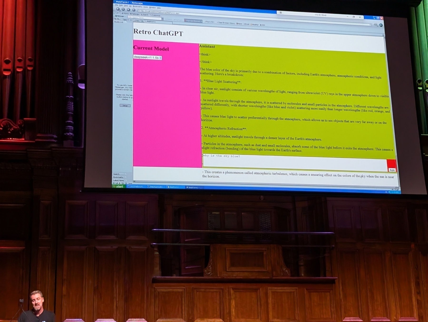 Auto-generated description: A lecturer stands in front of a large projected screen displaying a webpage titled Retro ChatGPT with colorful sections of text.