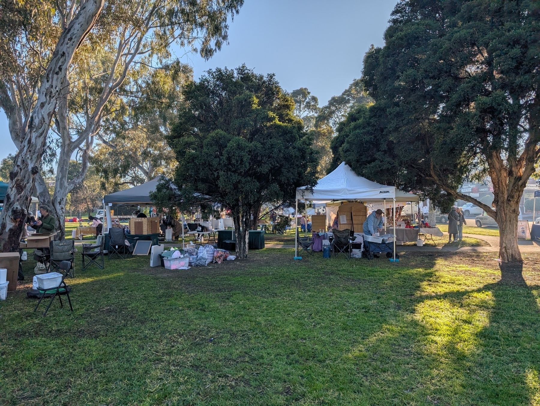 Auto-generated description: A small outdoor market setup features tents, tables, and trees in a grassy area.