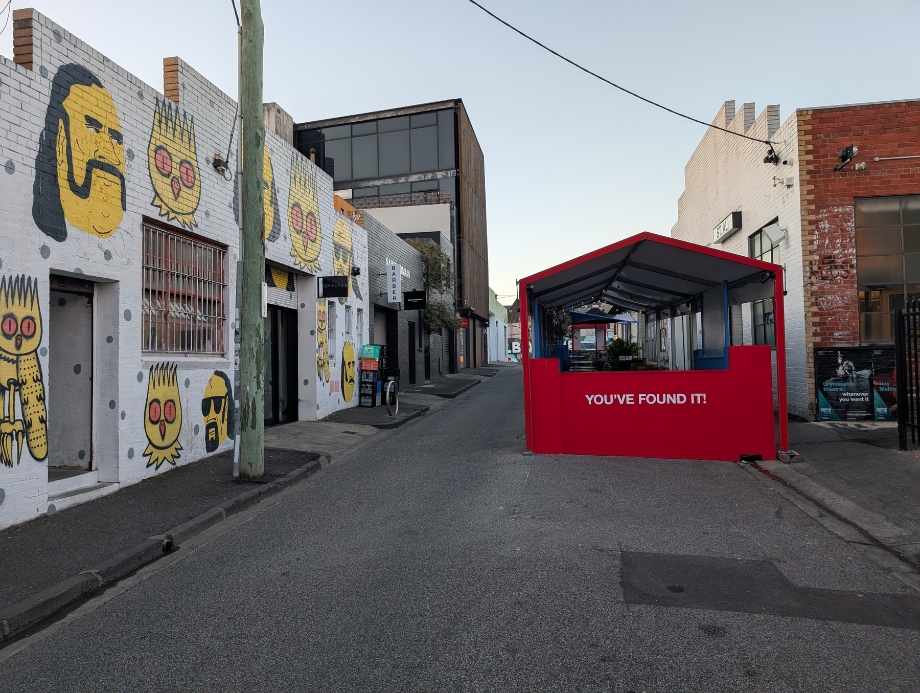 Auto-generated description: A narrow urban alleyway with colourful graffiti on the walls and a bright red kiosk with the text YOU'VE FOUND IT! at the end.