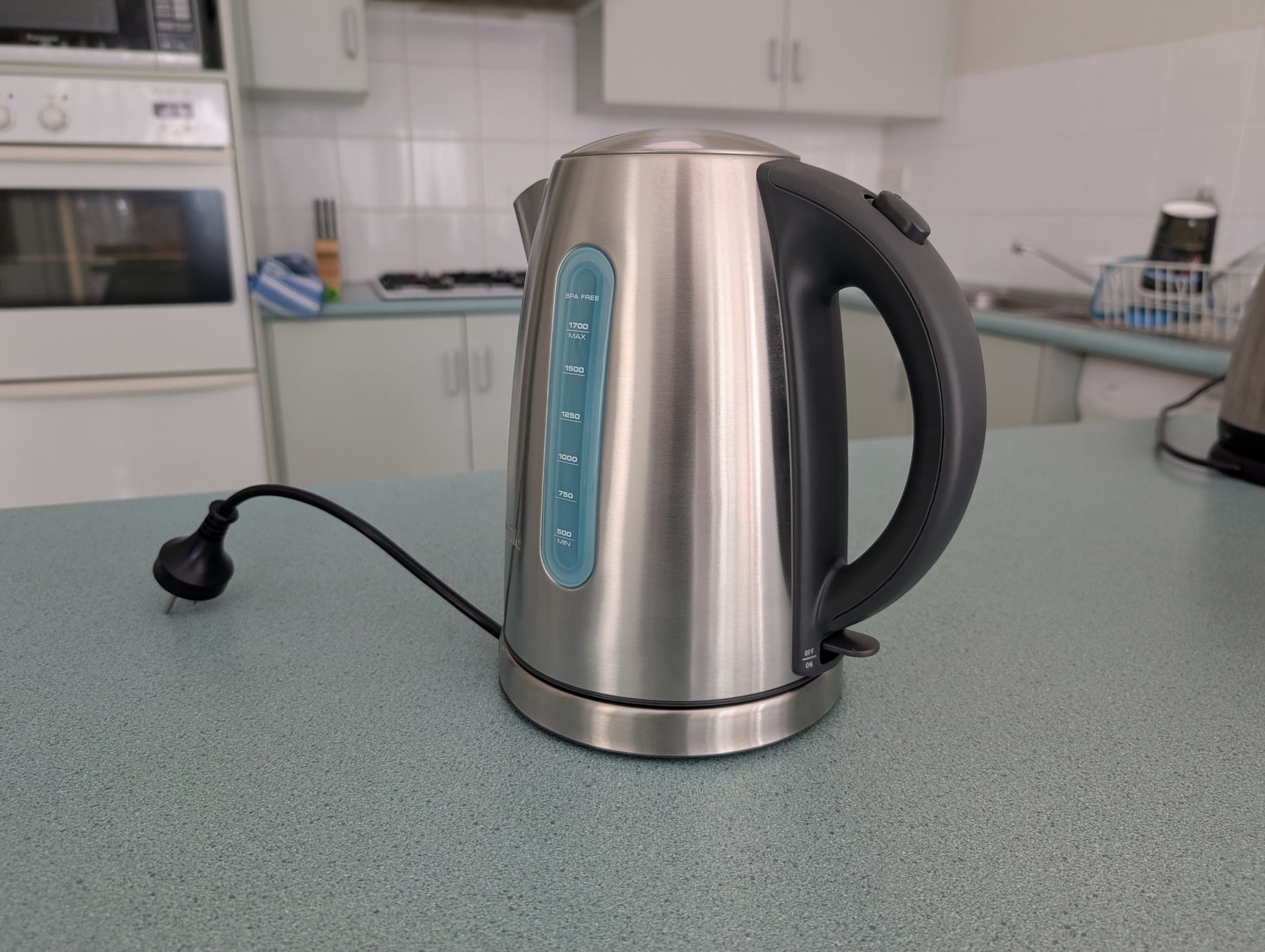 A stainless steel kettle sitting on its base on a kitchen bench.