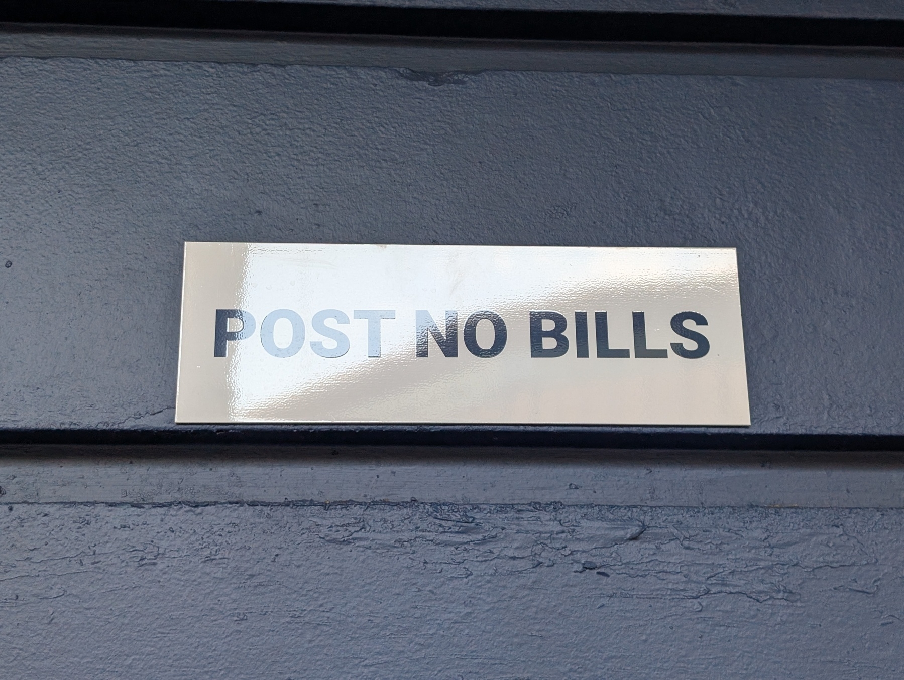 A white sign on a blue building with the text POST NO BILLS