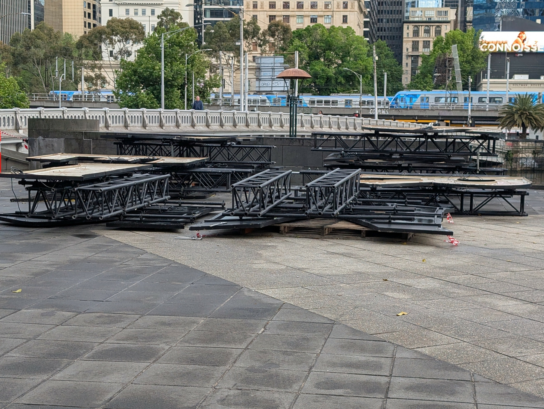 Large letters and scaffolding laying on the ground with a bridge behind it.