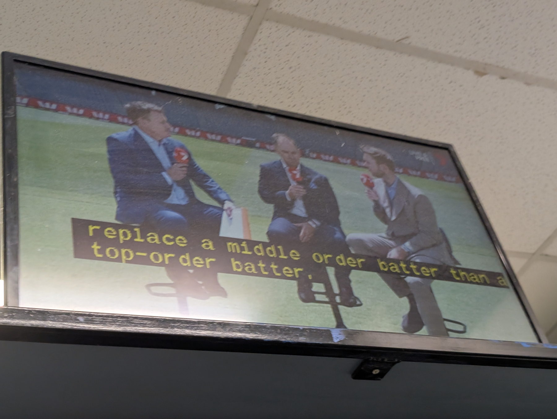 Three people are sitting on stools, holding microphones, with a caption about cricket strategy displayed on the screen.