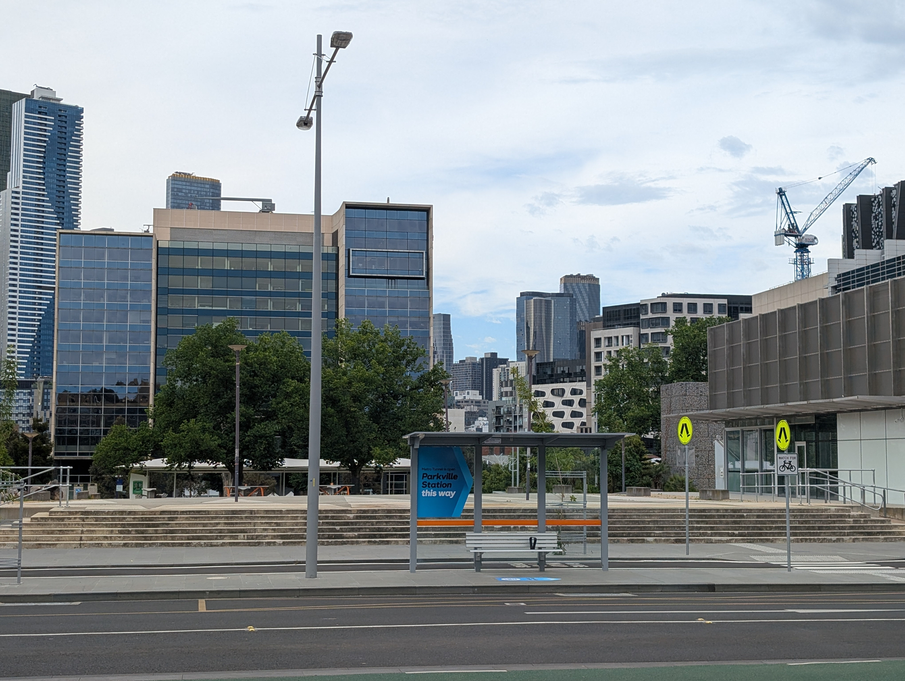 Auto-generated description: A cityscape with modern buildings, a bus shelter, and a construction crane in the background.