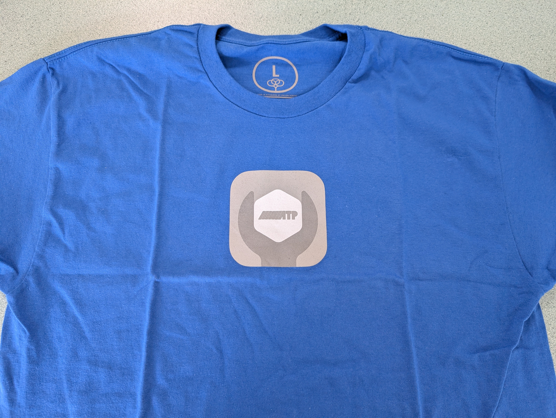 Auto-generated description: A blue T-shirt features a logo of hands holding a hexagonal shape.