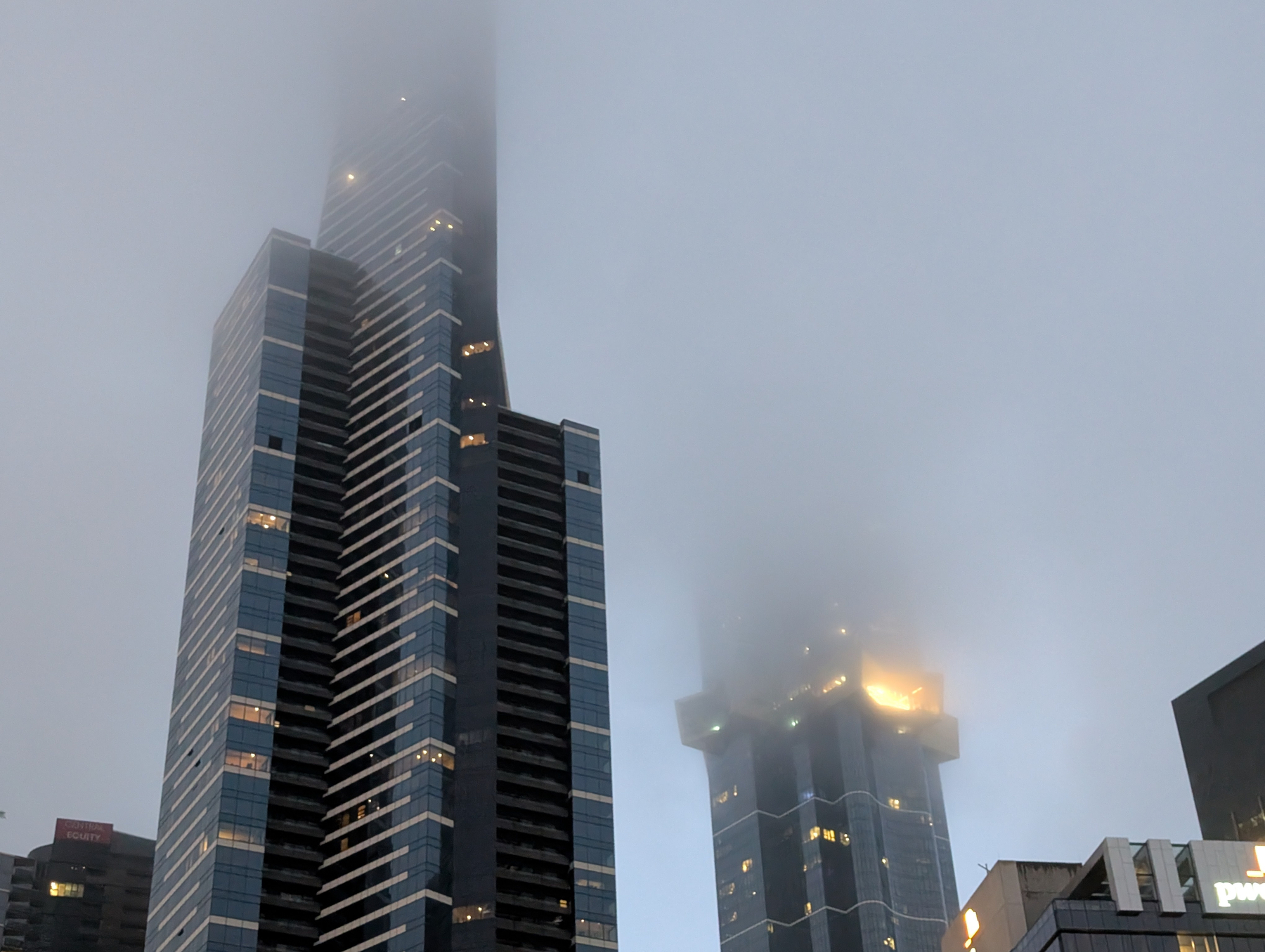 Auto-generated description: Two modern skyscrapers partially obscured by fog with the top levels disappearing into the mist.