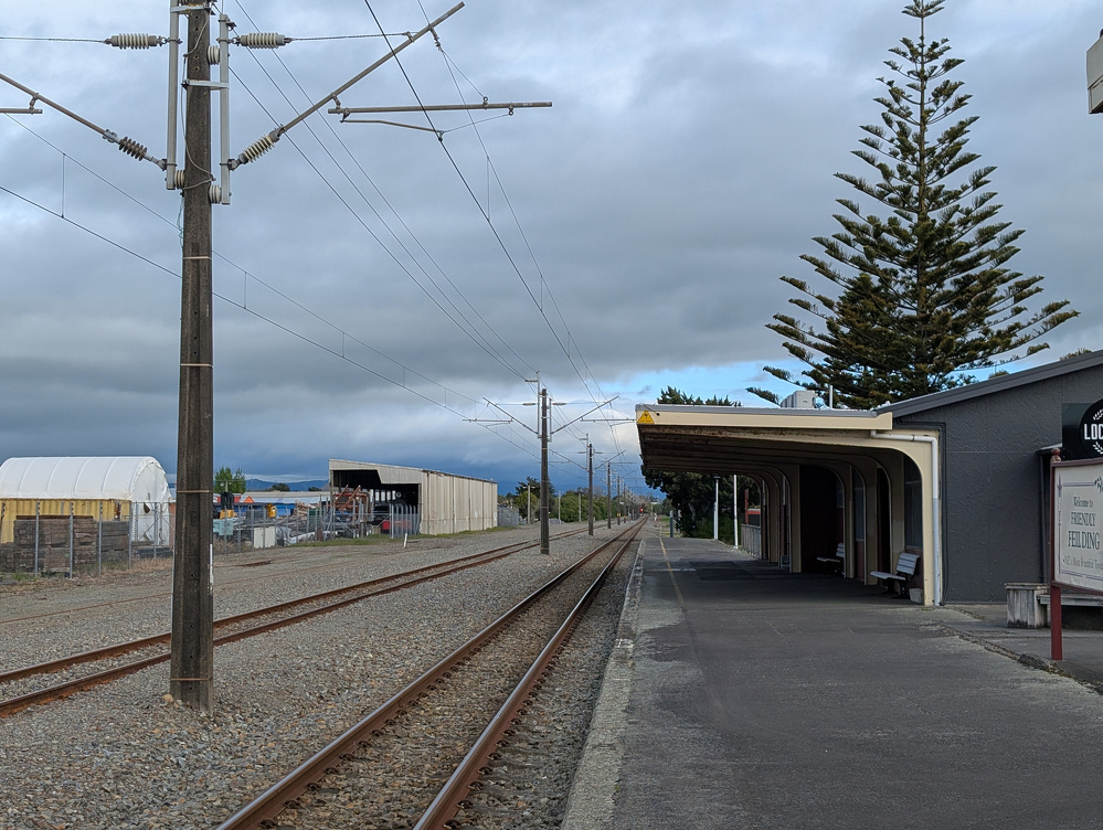 Auto-generated description: A quiet train station platform is seen beside railway tracks stretching into the distance under a cloudy sky.