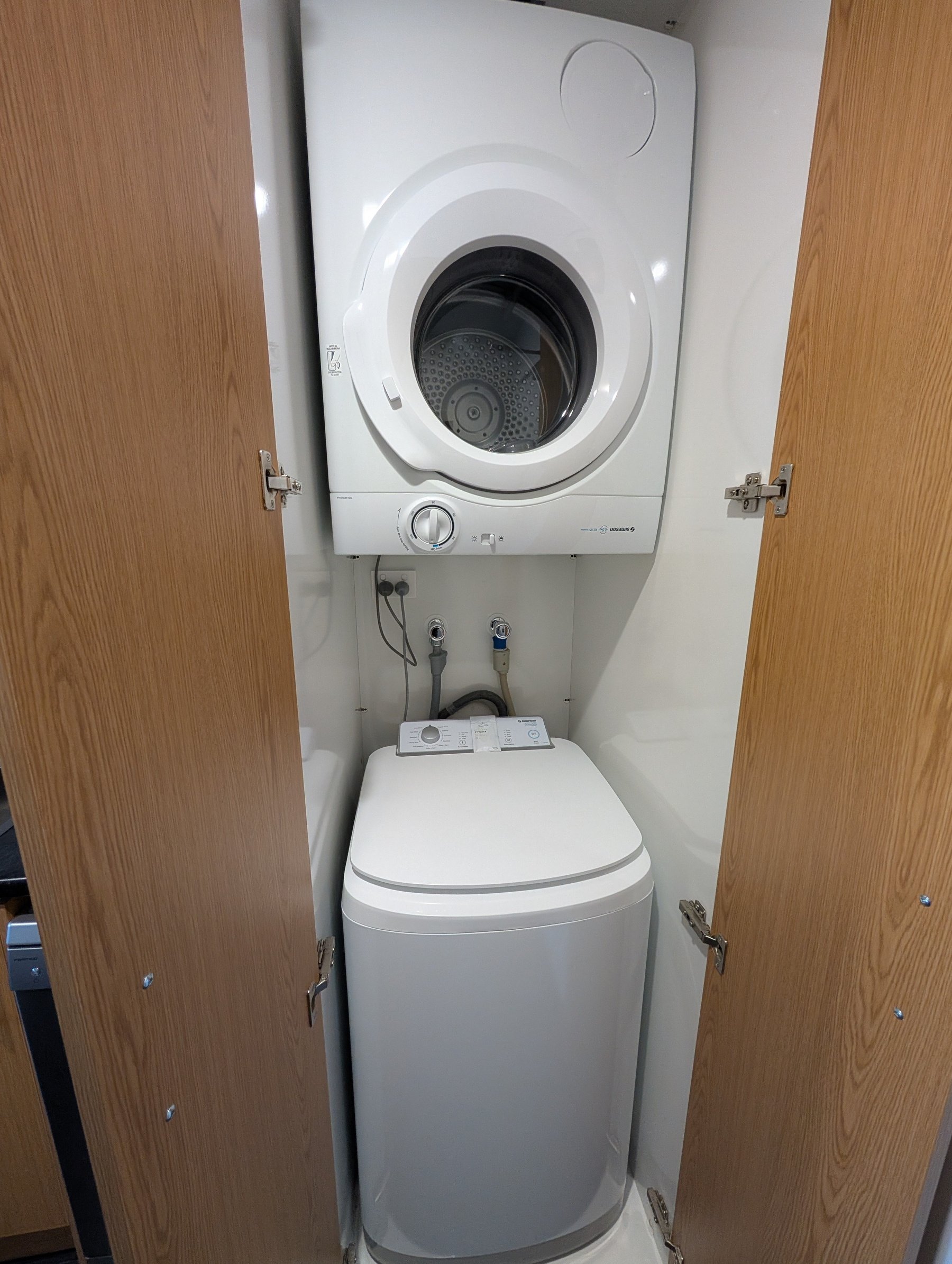 A compact laundry setup with a front-loading dryer stacked above a top-loading washing machine enclosed within wooden doors.