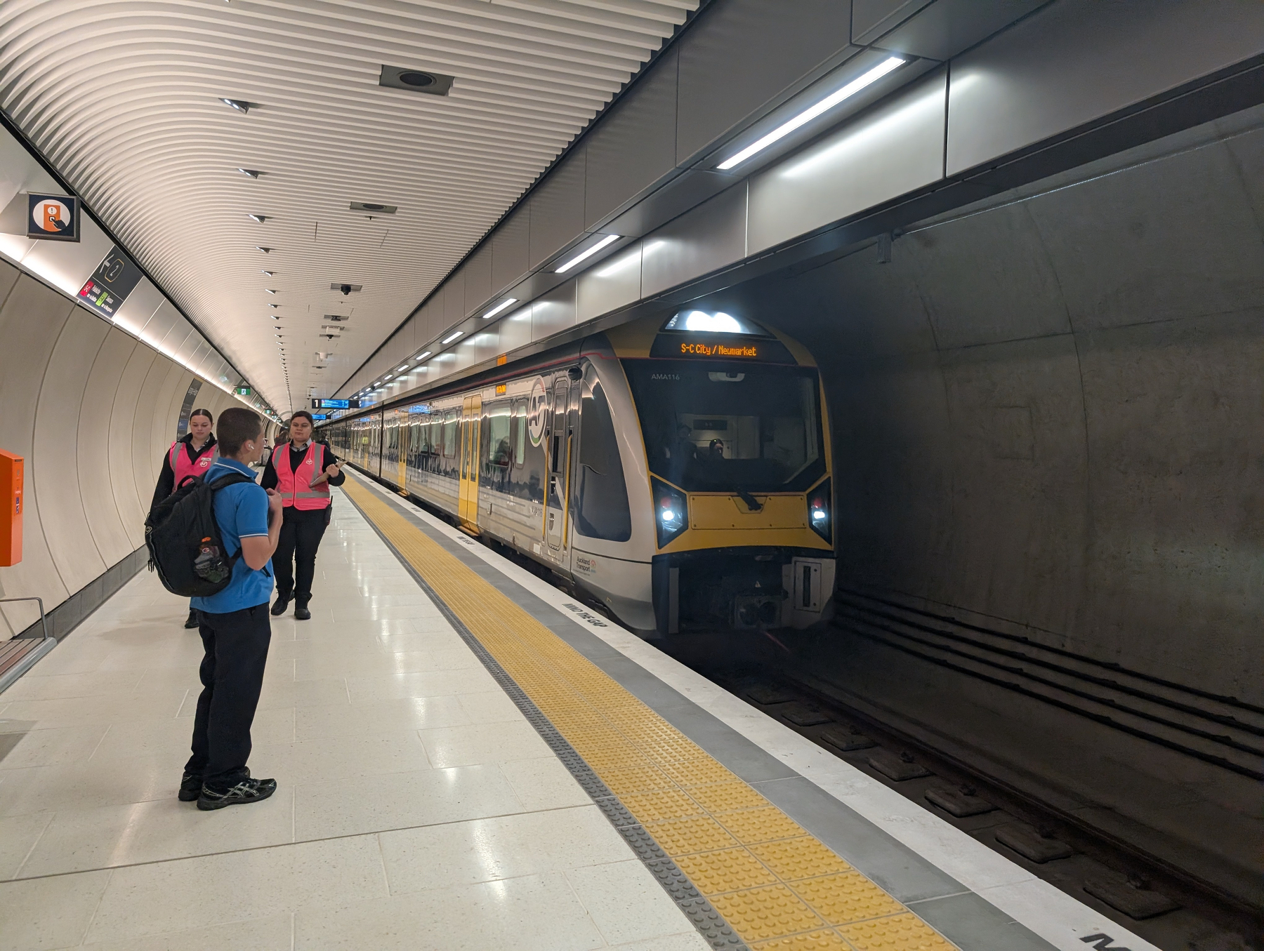Auto-generated description: A modern train has arrived at an underground station where passengers and staff are waiting on the platform.