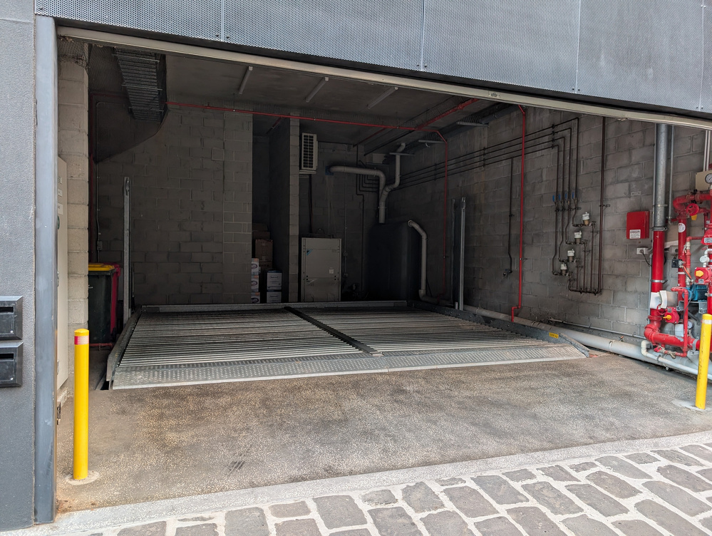 An empty garage with industrial equipment and yellow safety bollards at the entrance, with a lift as a floor.