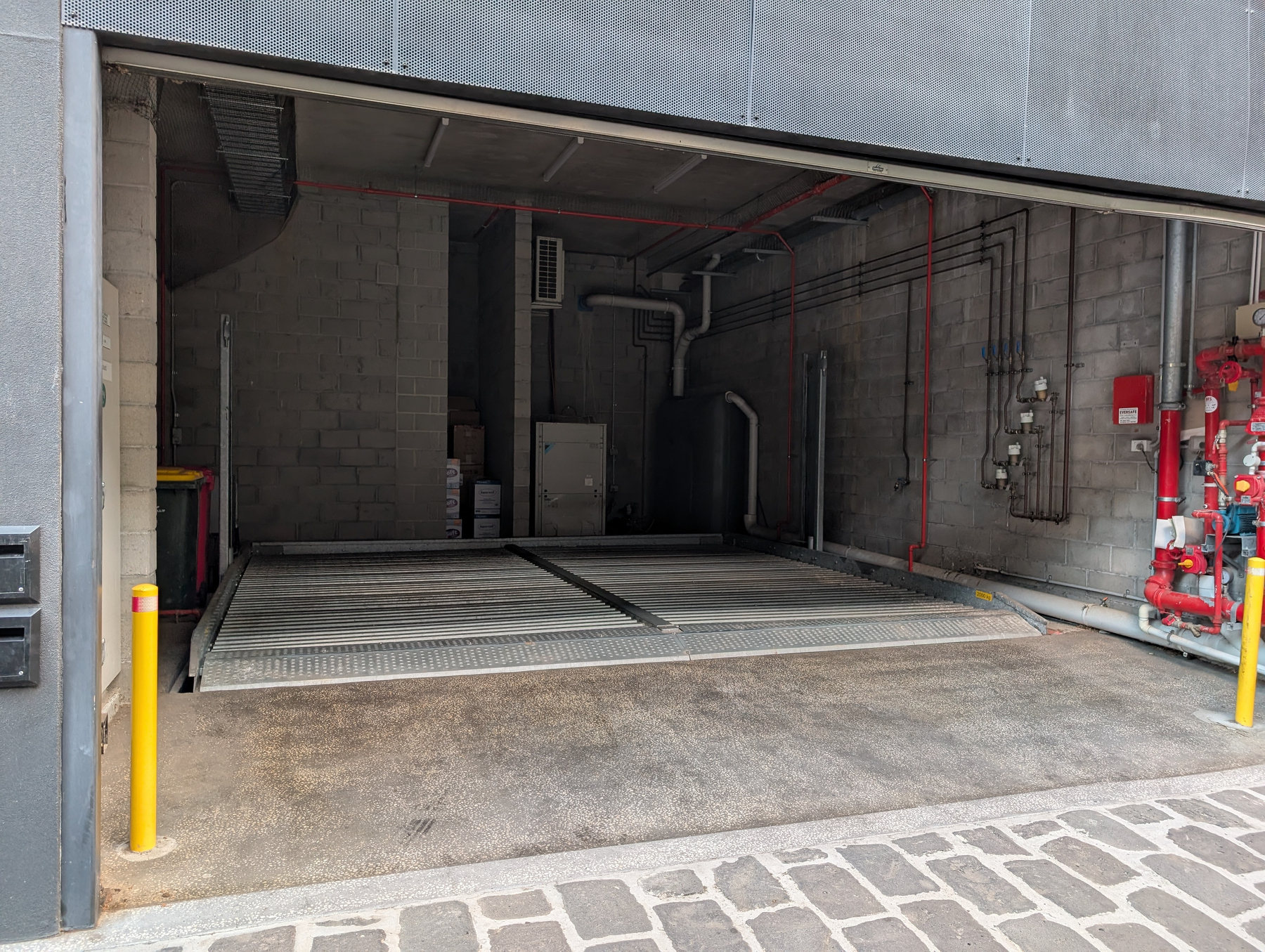 An empty garage with industrial equipment and yellow safety bollards at the entrance, with a lift as a floor.