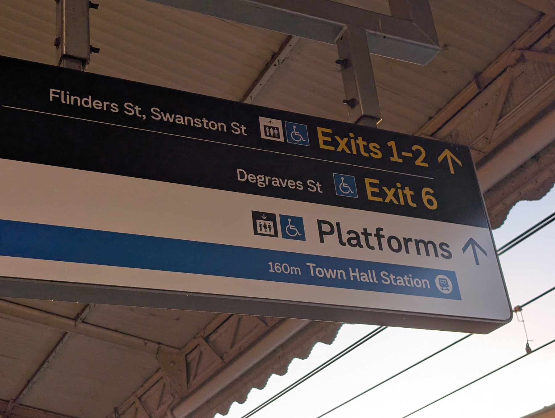 Auto-generated description: A directional sign at a train station points towards exits 1-2, exit 6, and platforms, with specific references to Flinders St, Swanston St, Degraves St, and Town Hall Station.