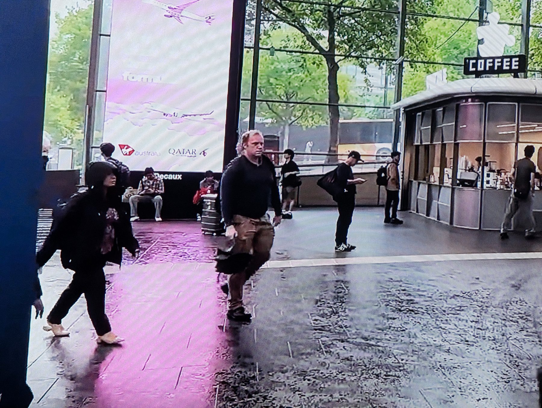 Auto-generated description: People are walking inside a spacious, modern building with a large window and a coffee shop visible in the background.