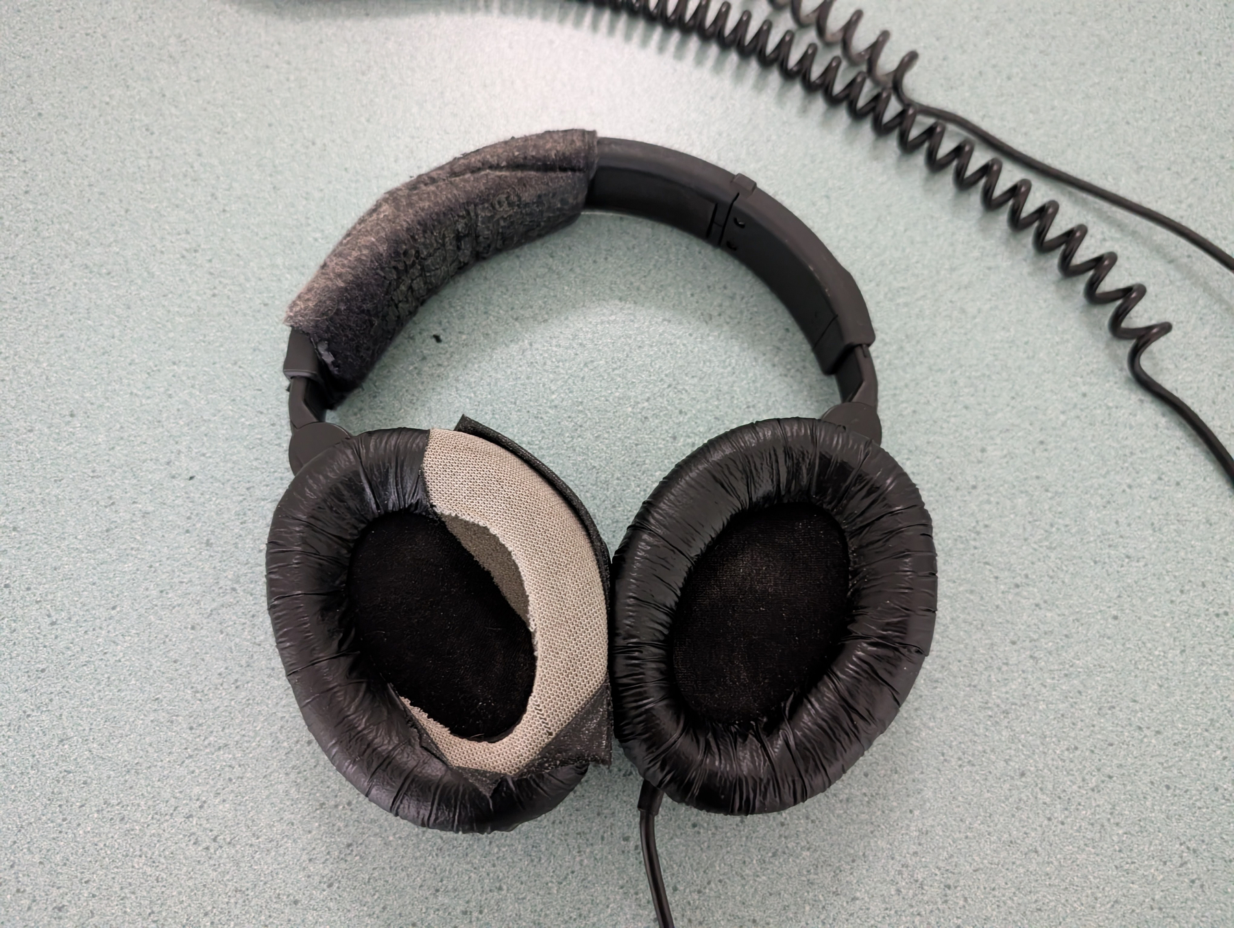 Auto-generated description: Headphones with worn and frayed ear cushions are resting on a textured surface.