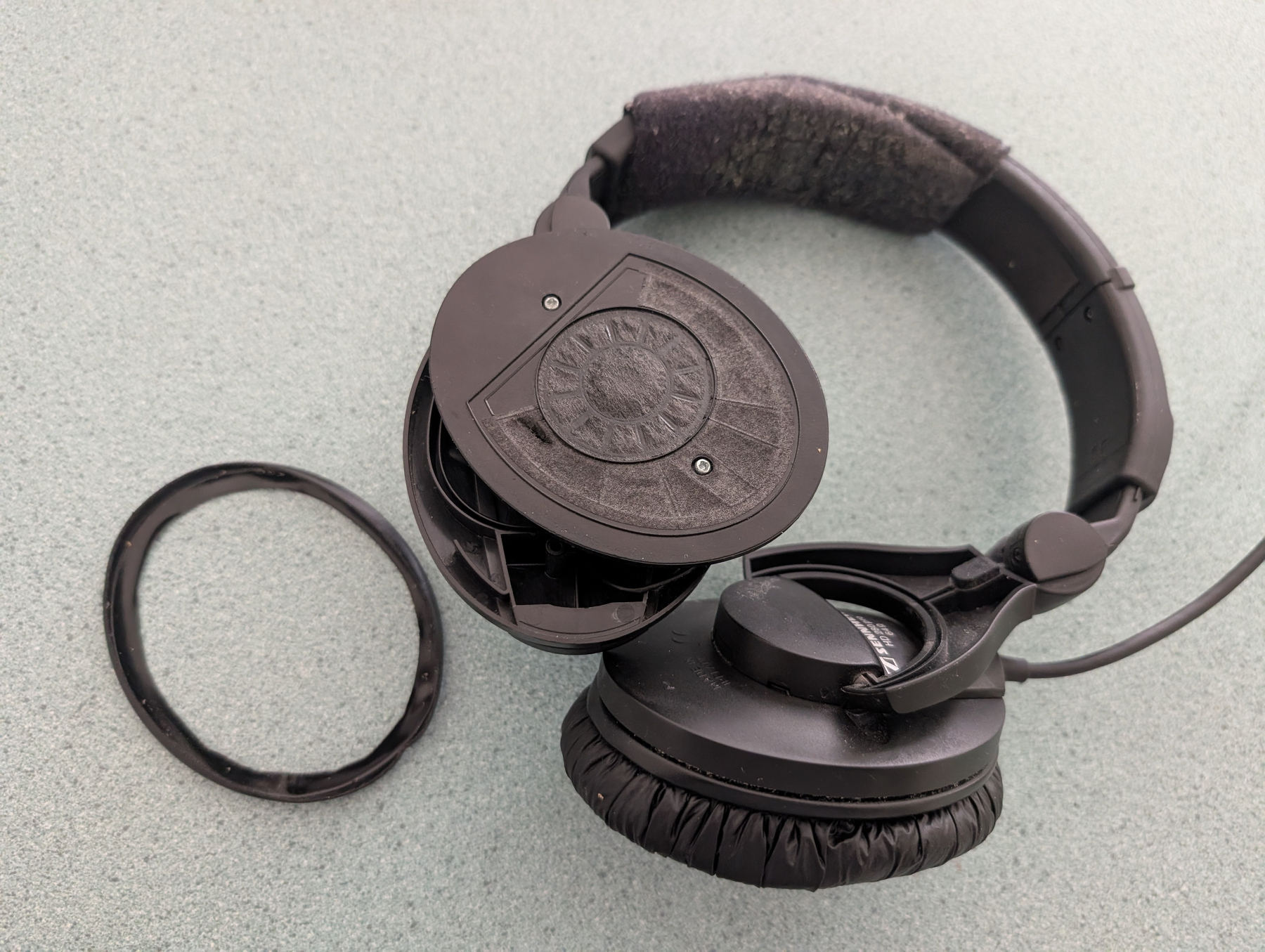 Auto-generated description: A pair of black headphones with one ear cup detached and its cover removed sits on a light-colored surface.