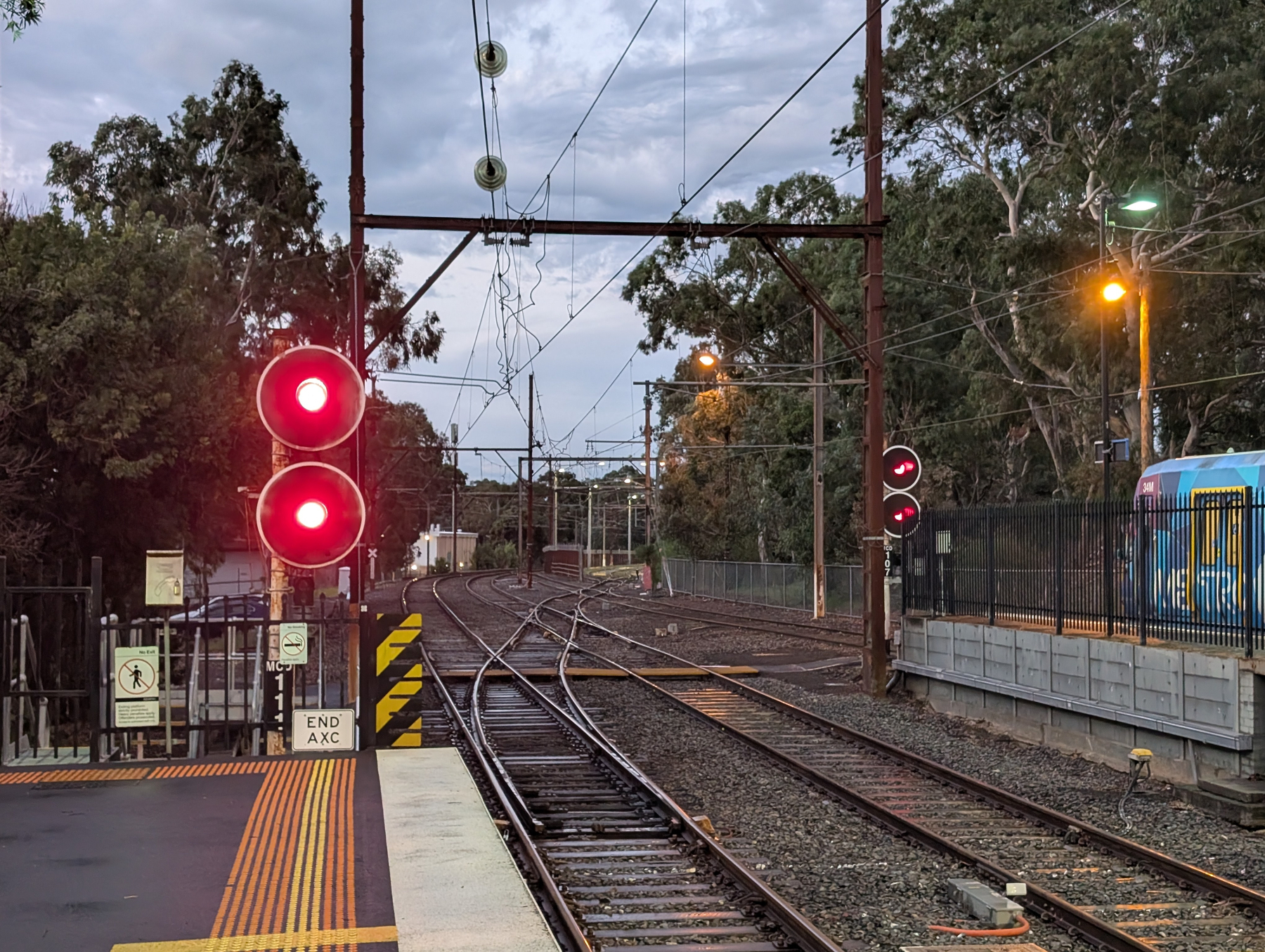 Auto-generated description: A railway station is visible with red signal lights, multiple tracks, and a train approaching in the background.