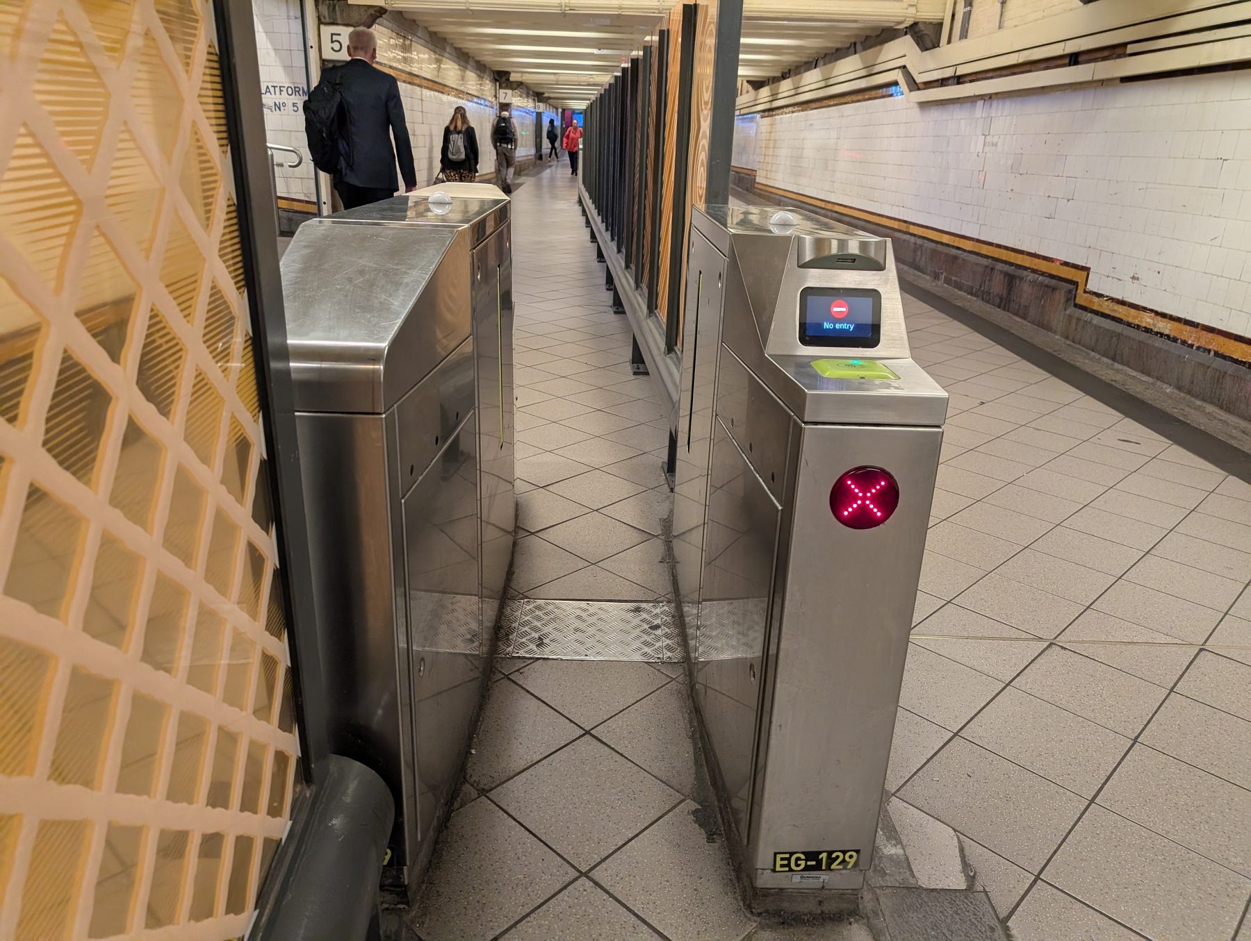 Auto-generated description: A subway turnstile entrance with people walking through the corridor in the background.