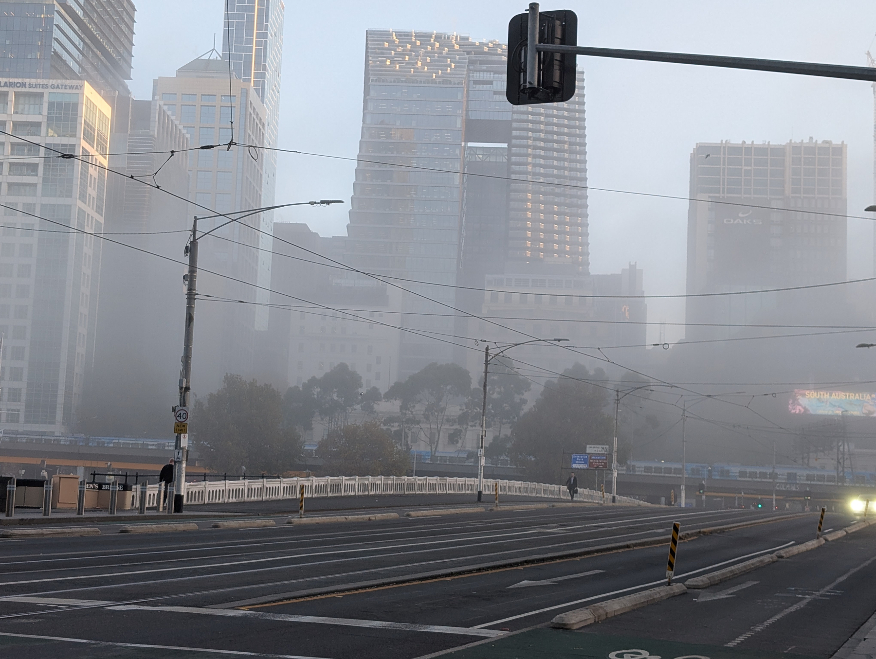 Auto-generated description: A foggy cityscape features modern skyscrapers and an empty street with a few visible vehicles and pedestrians.