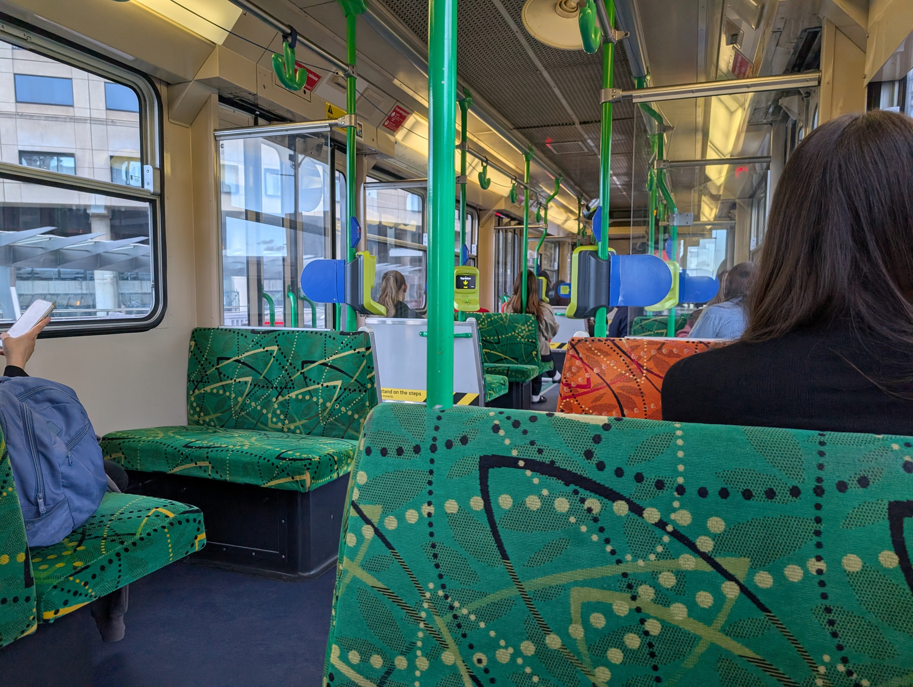 A person is riding a tram with green-patterned seats, looking out the window.