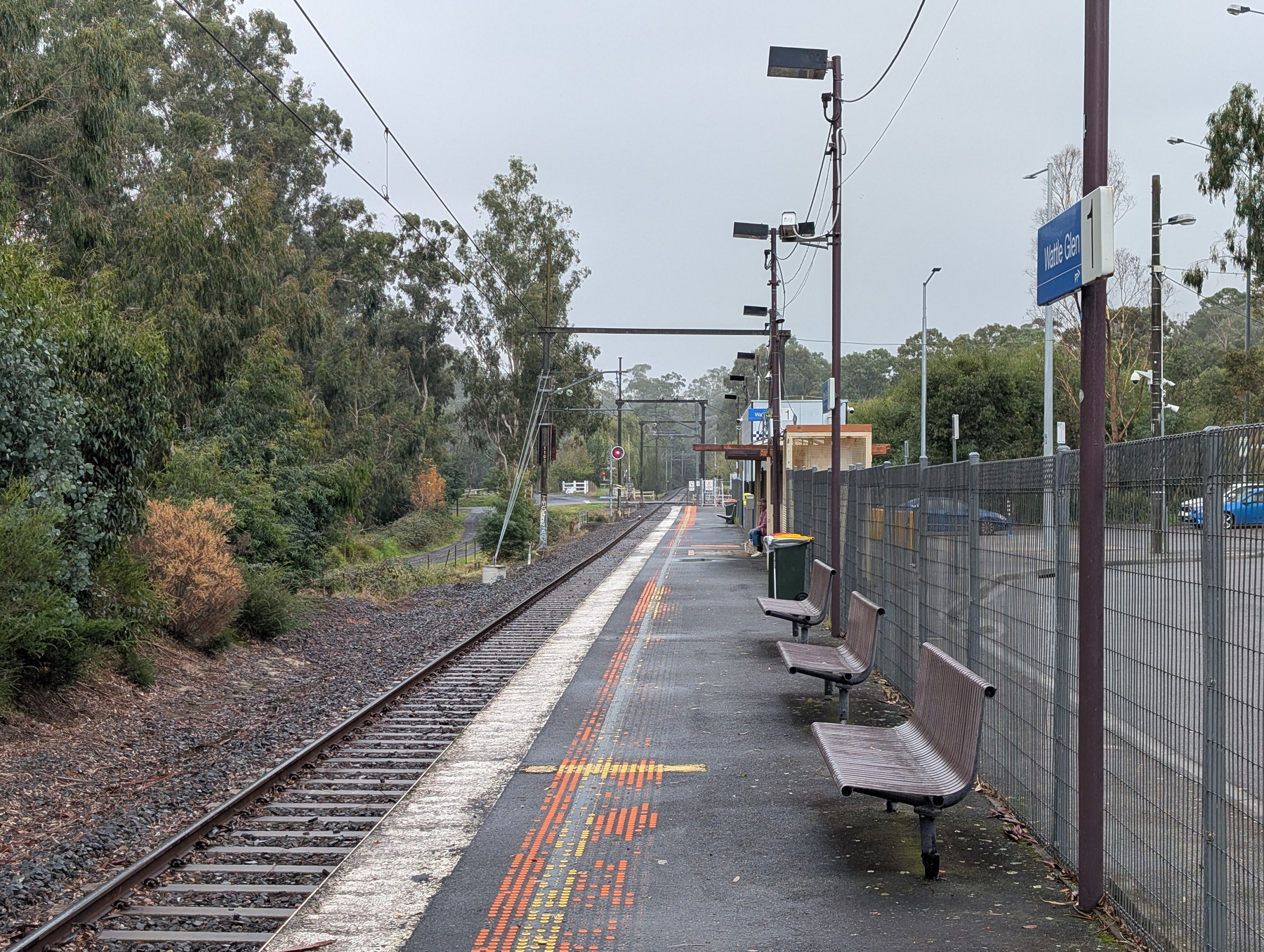 Auto-generated description: A quiet, empty train platform with benches and greenery on a cloudy day.
