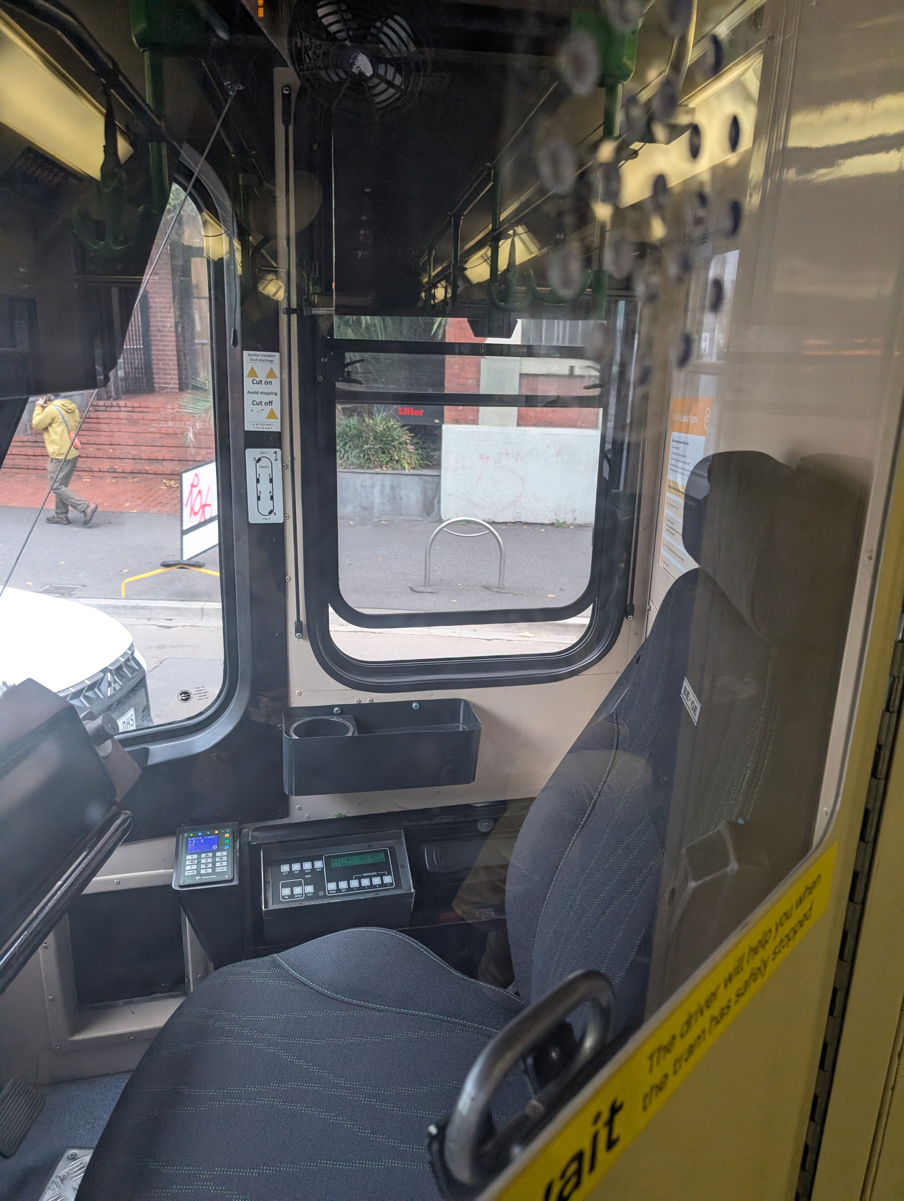 An empty driver's seat inside a tram is visible, with a view of the street and a pedestrian outside.
