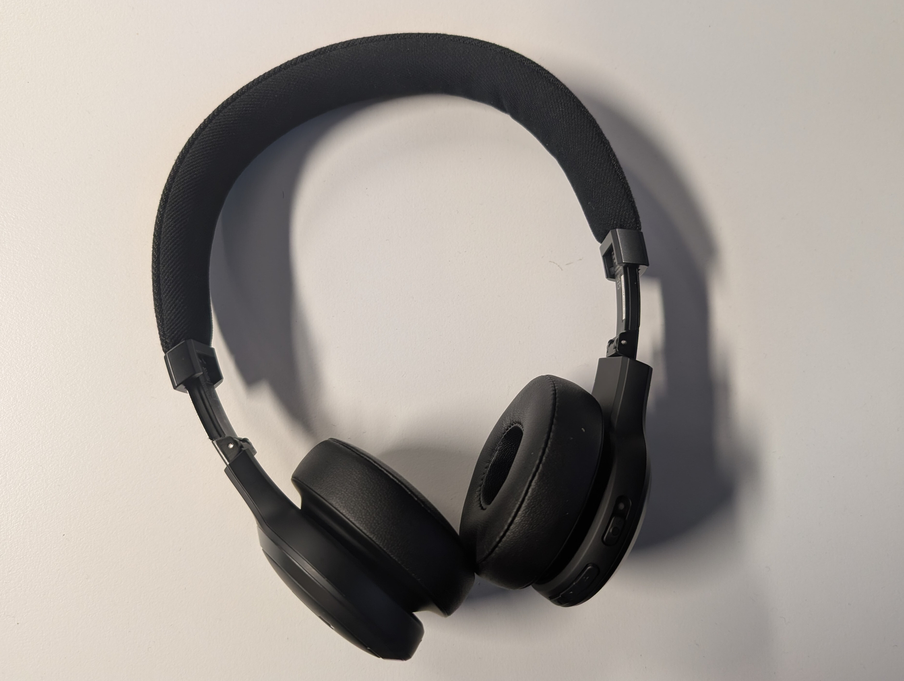 Auto-generated description: A pair of black over-ear headphones with a padded headband is resting on a white surface.