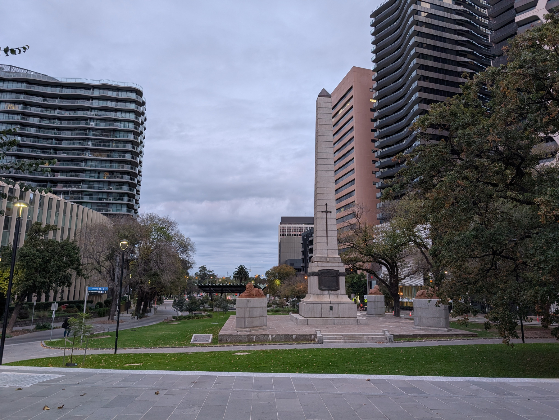 Auto-generated description: A cityscape features a mixture of modern high-rise buildings, a central monument with a column, and surrounding greenery on a cloudy day.