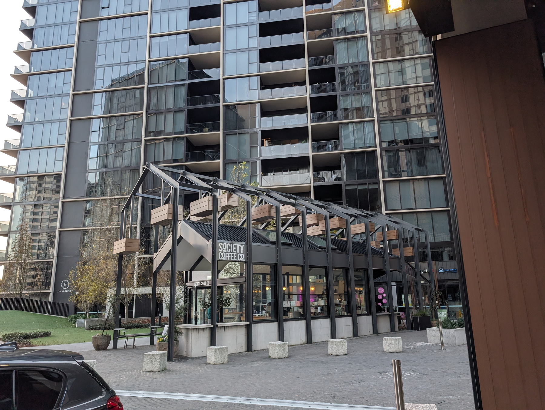 Auto-generated description: A modern coffee shop with a glass and metal structure is situated in front of a tall residential building.
