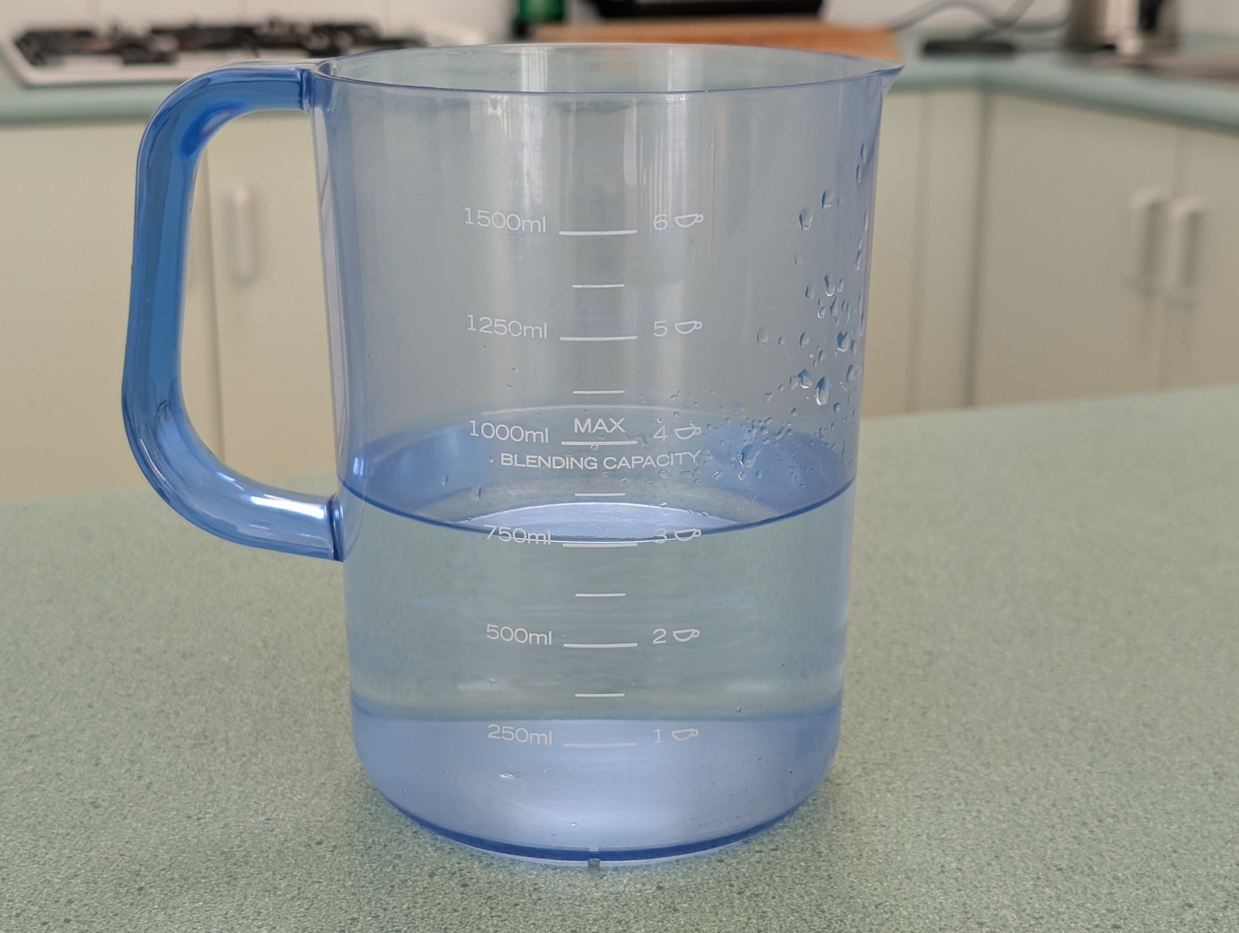 A transparent blue plastic measuring jug containing 750 ml of water is placed on a kitchen bench.