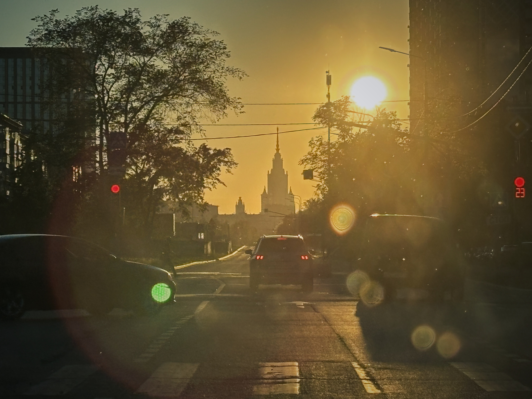 A city street at sunset features cars, silhouetted trees, and a prominent spire in the distance, with a warm golden light cast over the scene.